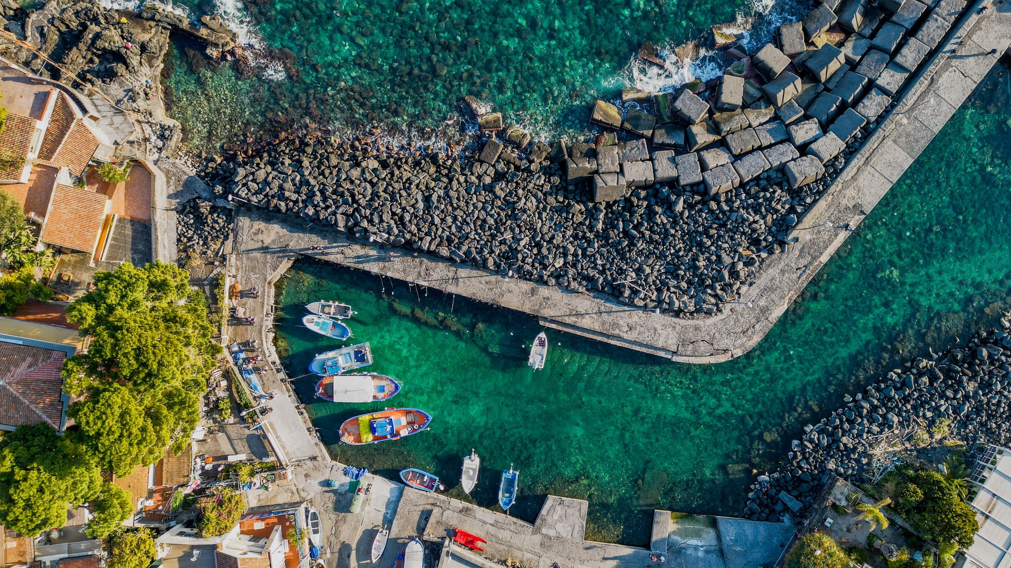 amex-magazin-catania-strand-boote In einer kleinen Bucht mit schwarzen Steinen und am Strand stehen bunte Boote.