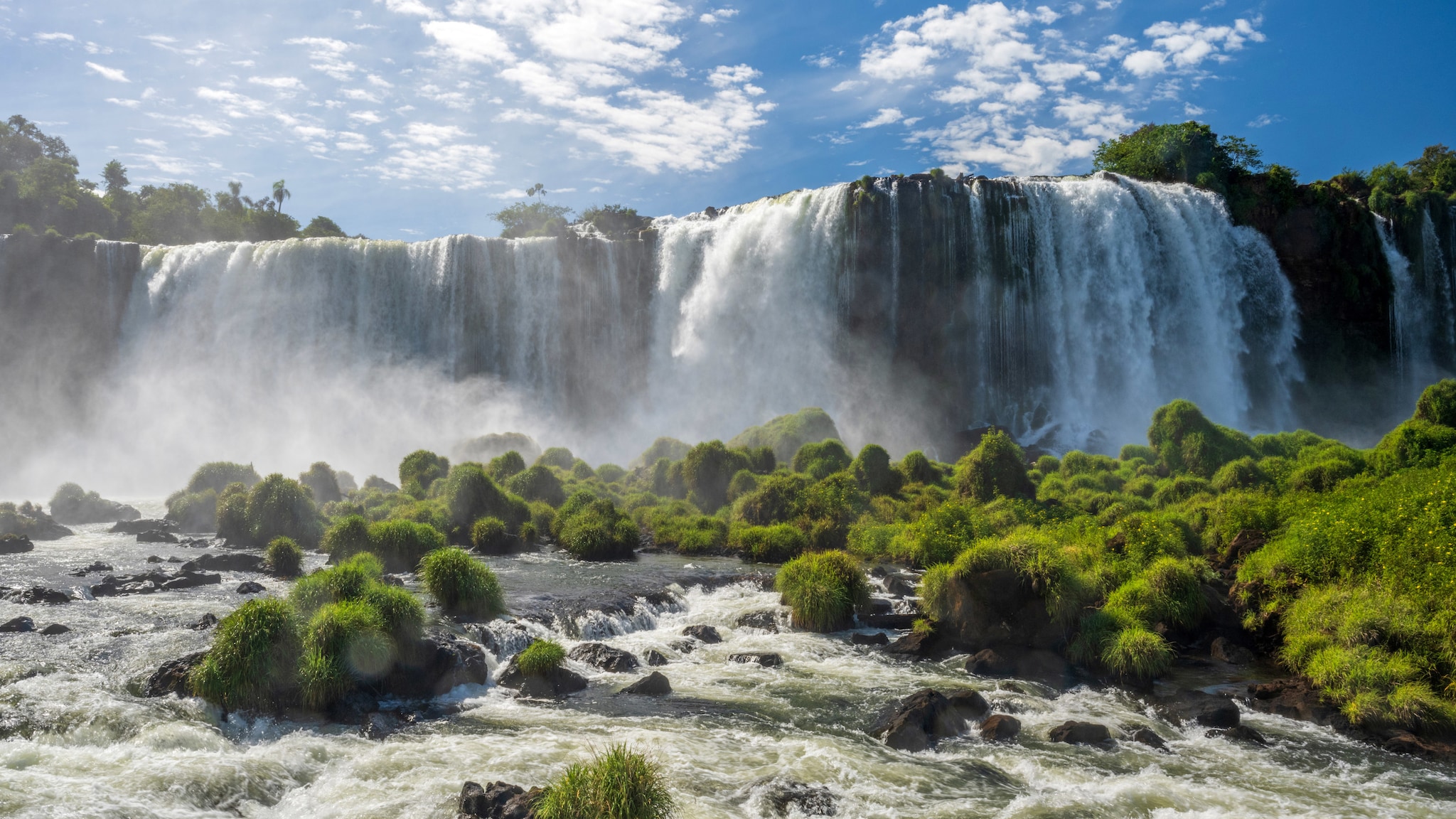 amex-magazin-wasserfaelle-brasilien-iguazu Von einer Berglandschaft fließt ein kilometerlanger Wasserfall.