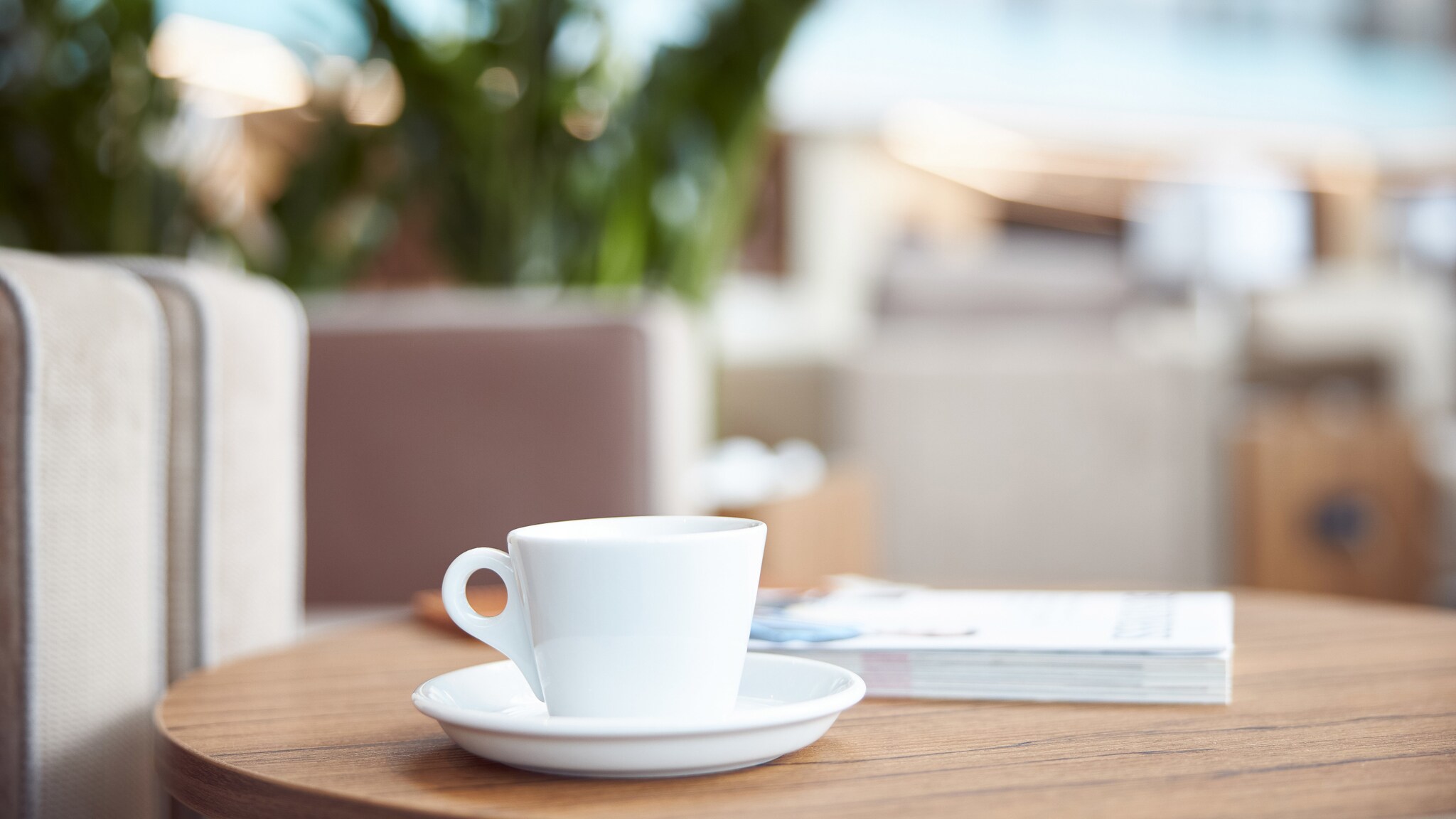 Auf einem Tisch steht eine weiße Tasse, daneben liegt ein Buch.