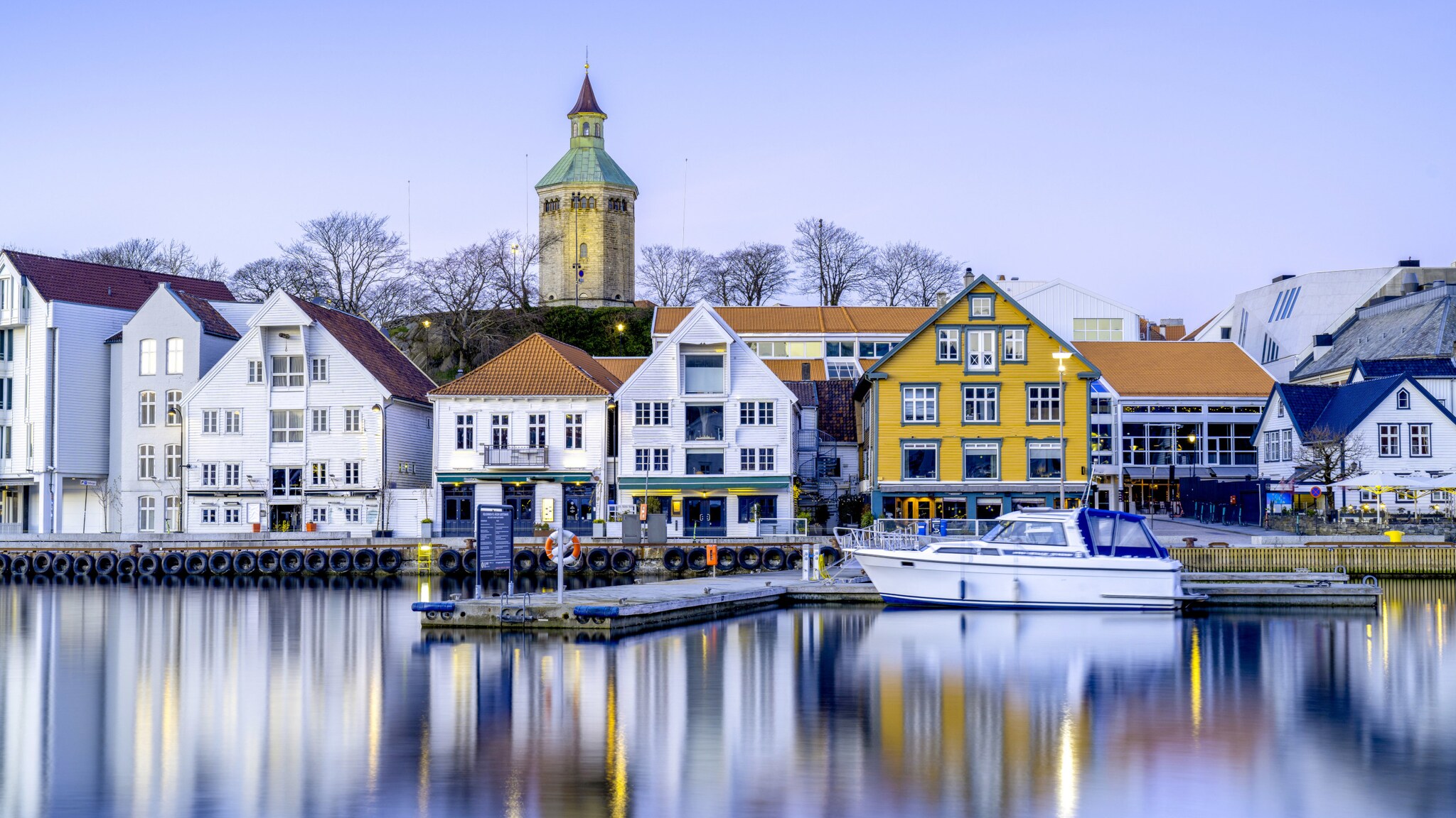 An einem ruhigen Fjord stehen weiße und bunte Häuser.