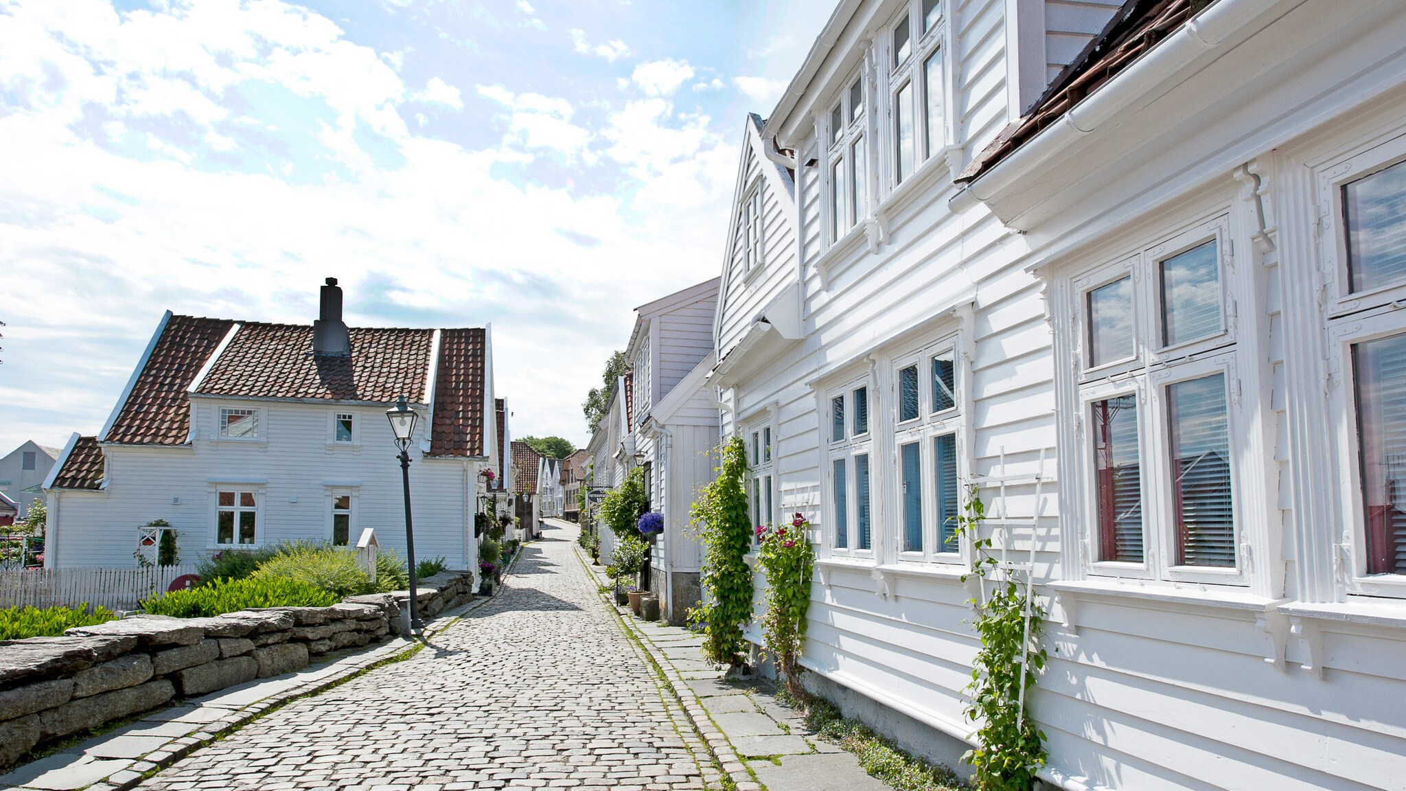 Neben einer Kopfsteinpflasterstraße stehen kleine, weiße Holzhäuser.