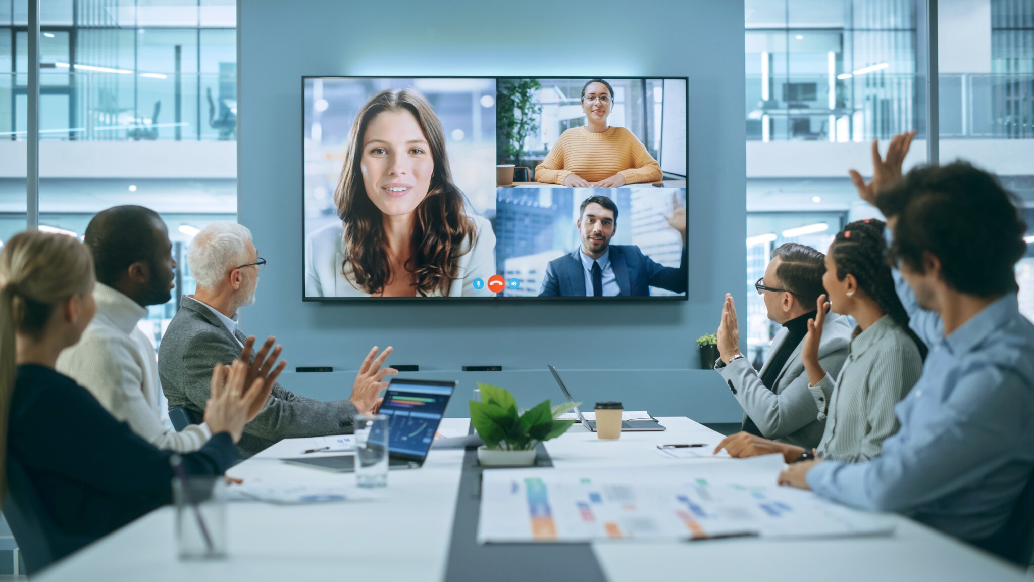 Während eines Meetings sind auf einem Monitor Personen zu sehen, die virtuell an einem Termin teilnehmen.
