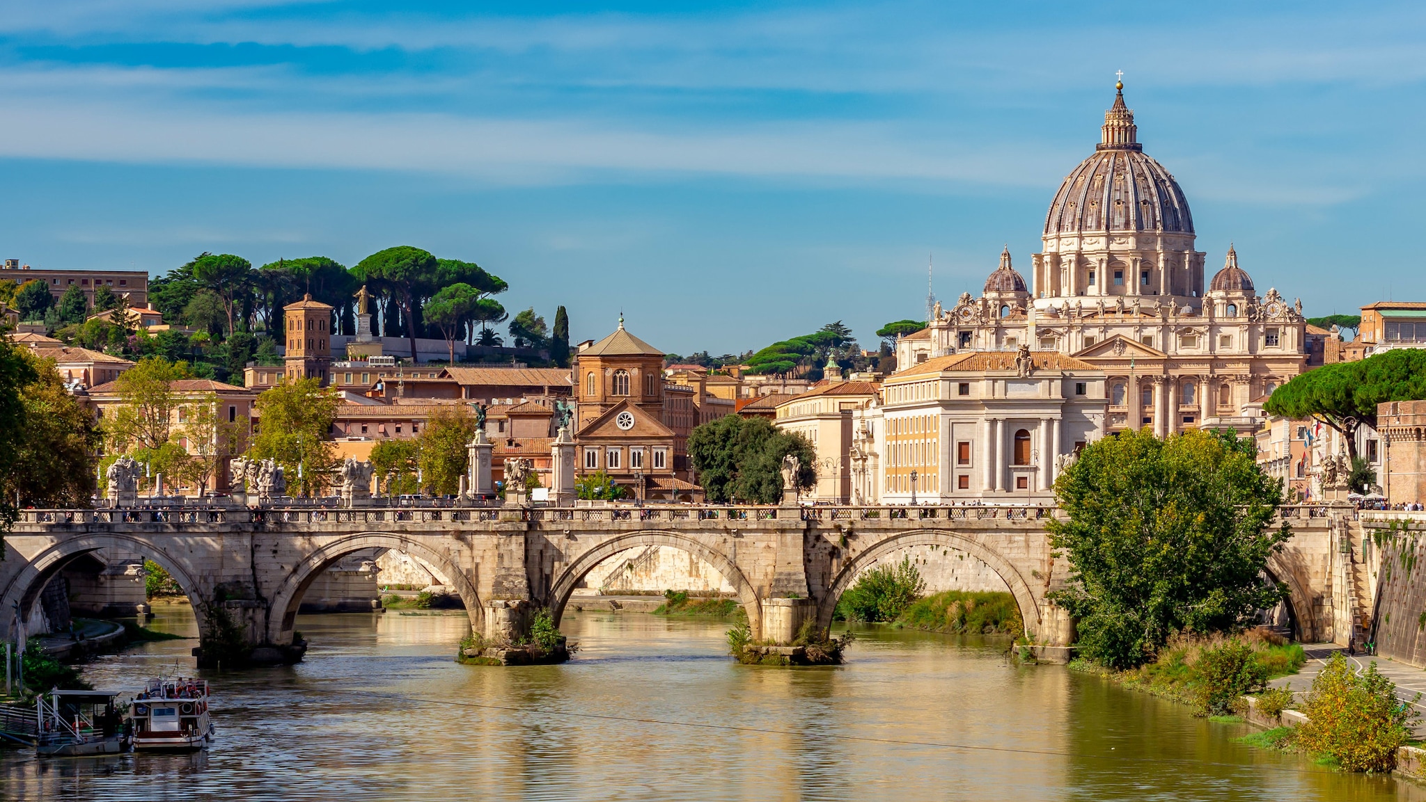 amex-magazin-rom-urlaub-fluss-bruecke Eine historische Brücke und Gebäude stehen an einem Fluss.
