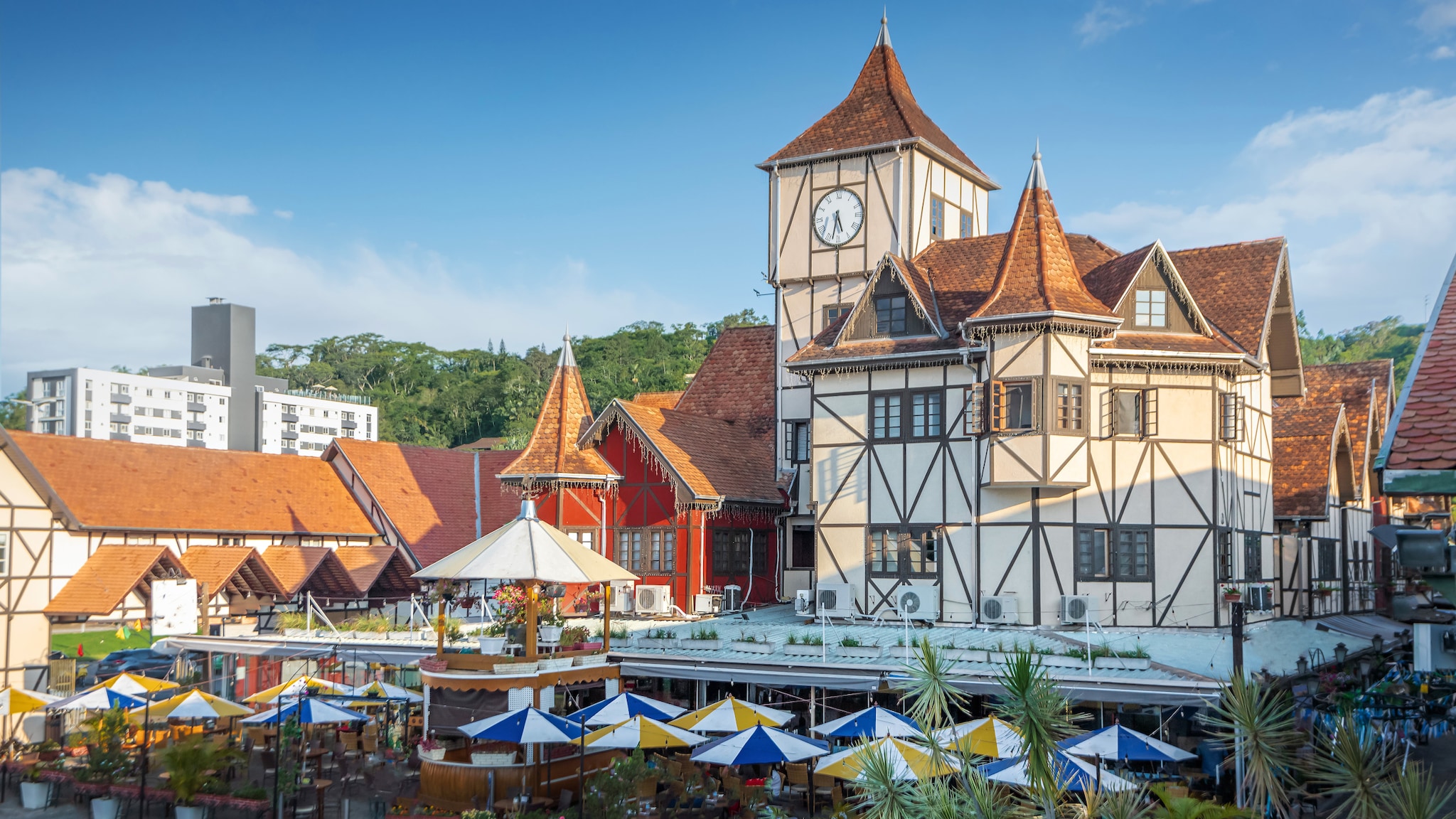 amex-magazin-blumenau-brasilien-sonnenschirme Auf einem Platz steht ein historisches Gebäude mit gestreiften Sonnenschirmen auf der Terrasse.