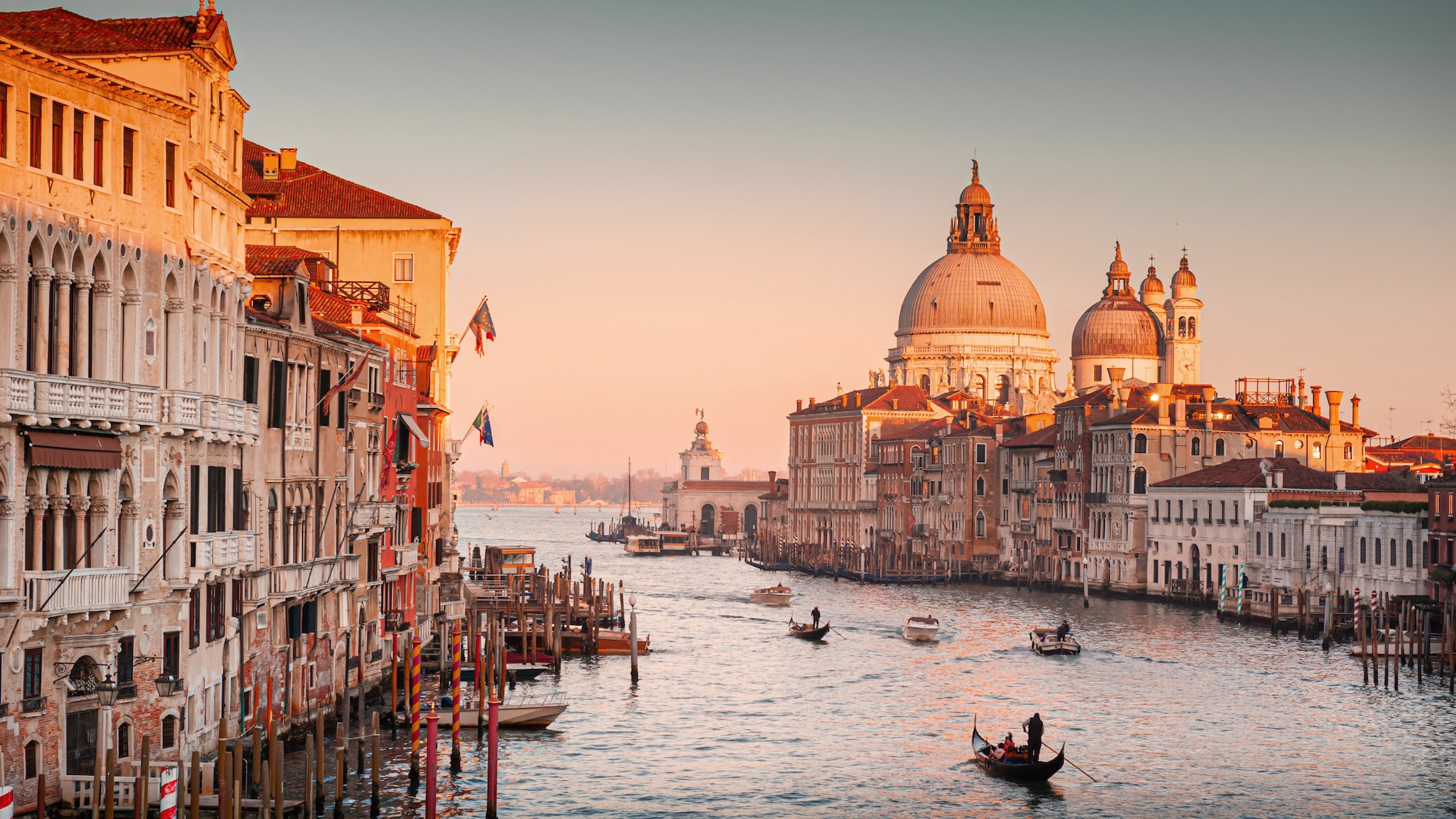 amex-magazin-venedig-urlaub-fluss-gondeln Auf einem großen Fluss fahren Gondeln, am Ufer stehen historische Gebäude.