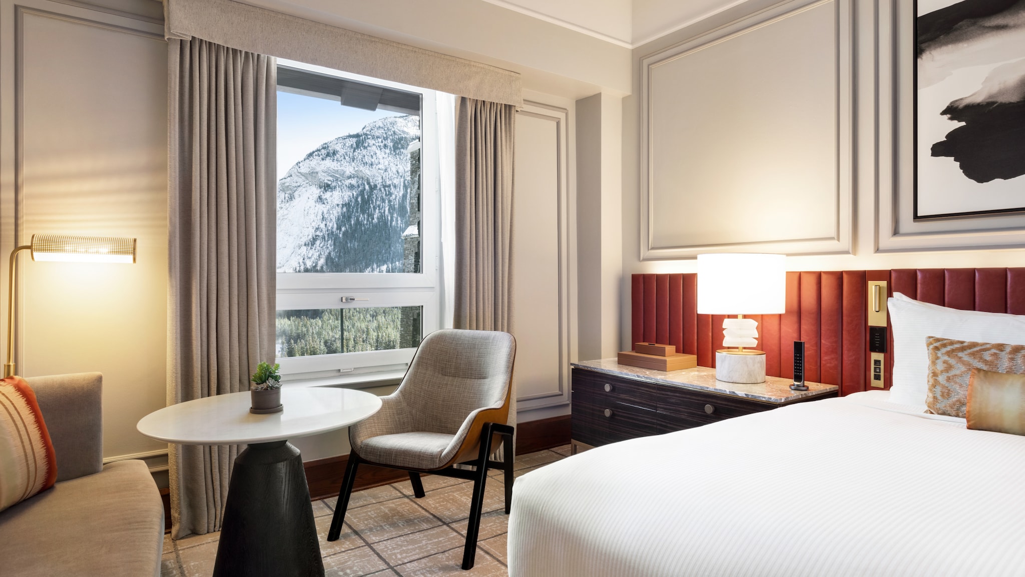 amex-magazin-urlaub-in-den-bergen-fairmont-hotelzimmer Modernes Hotelzimmer mit Fensterblick auf einen schneebedeckten Berghang.