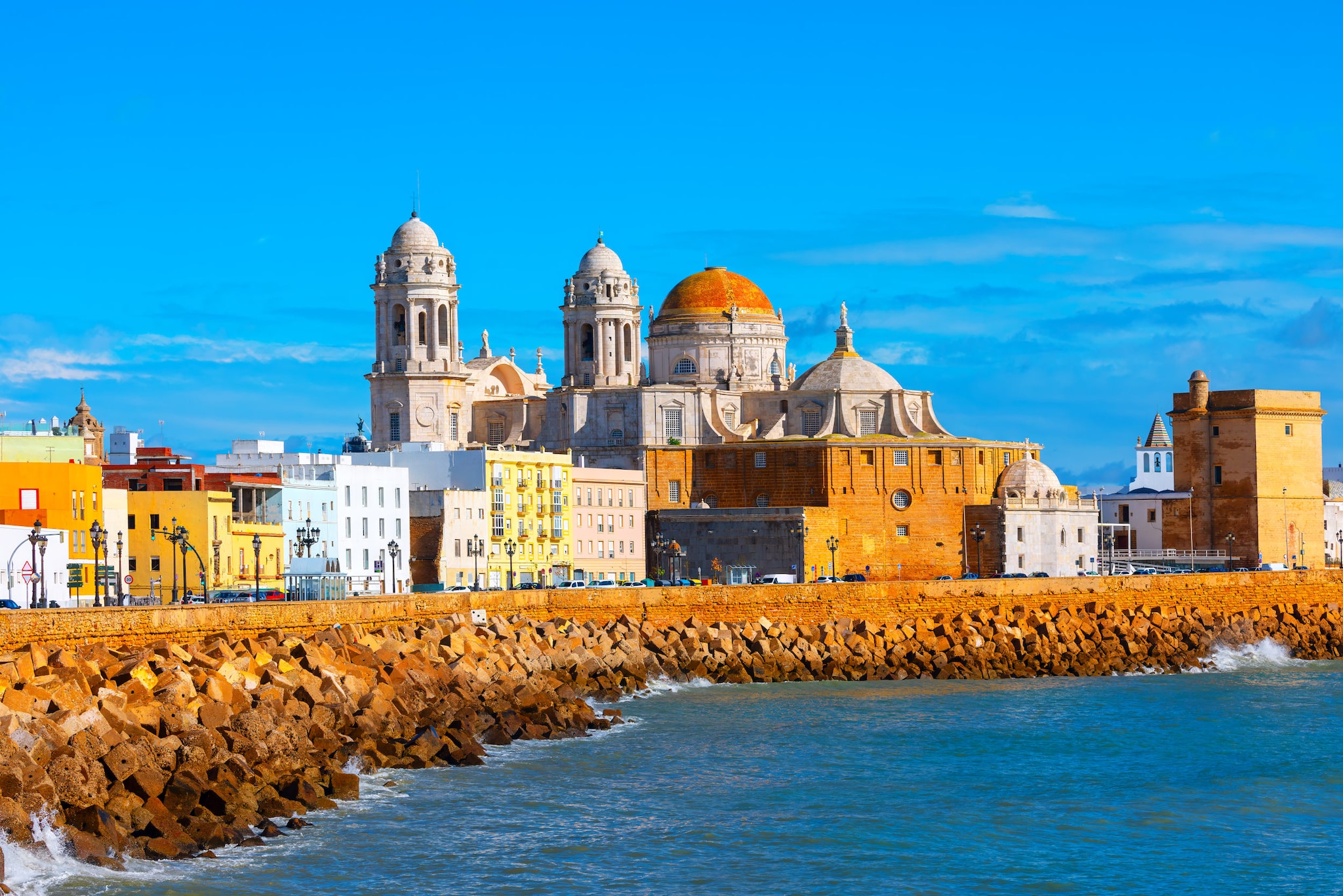 amex-magazin-cadiz-spanien-meer-stadt Stadt mit bunten Häusern und einer großen Kirche mit Kuppel direkt am Meer.
