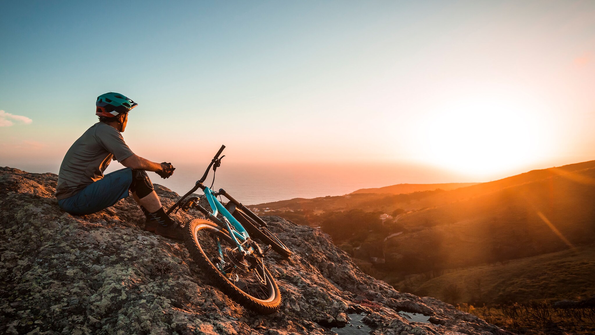 Ein Mann sitzt auf einem Berg, neben ihm liegt ein Mountainbike auf dem Boden.
