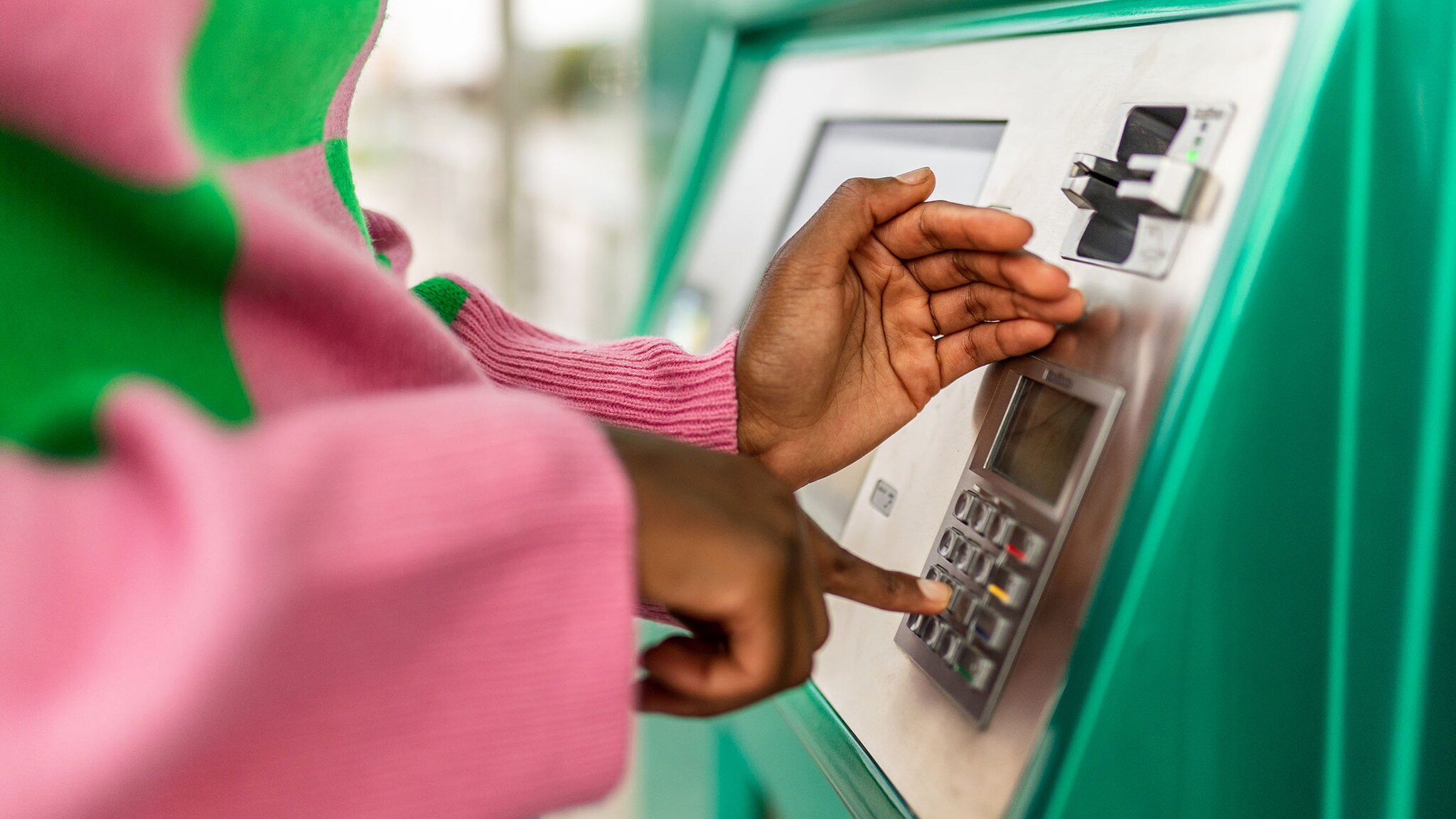 Nahaufnahme von zwei Händen einer Person am Geldautomaten; eine Hand bedient eine Taste, die andere wird schützend darüber gehalten.