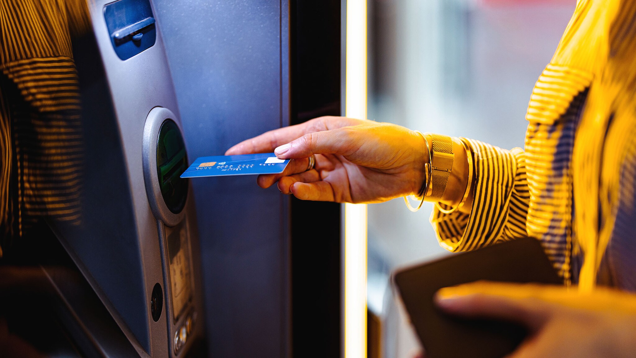 Nahaufnahme einer weiblichen Hand, die eine blaue Kreditkarte in einen Geldautomaten einführt.