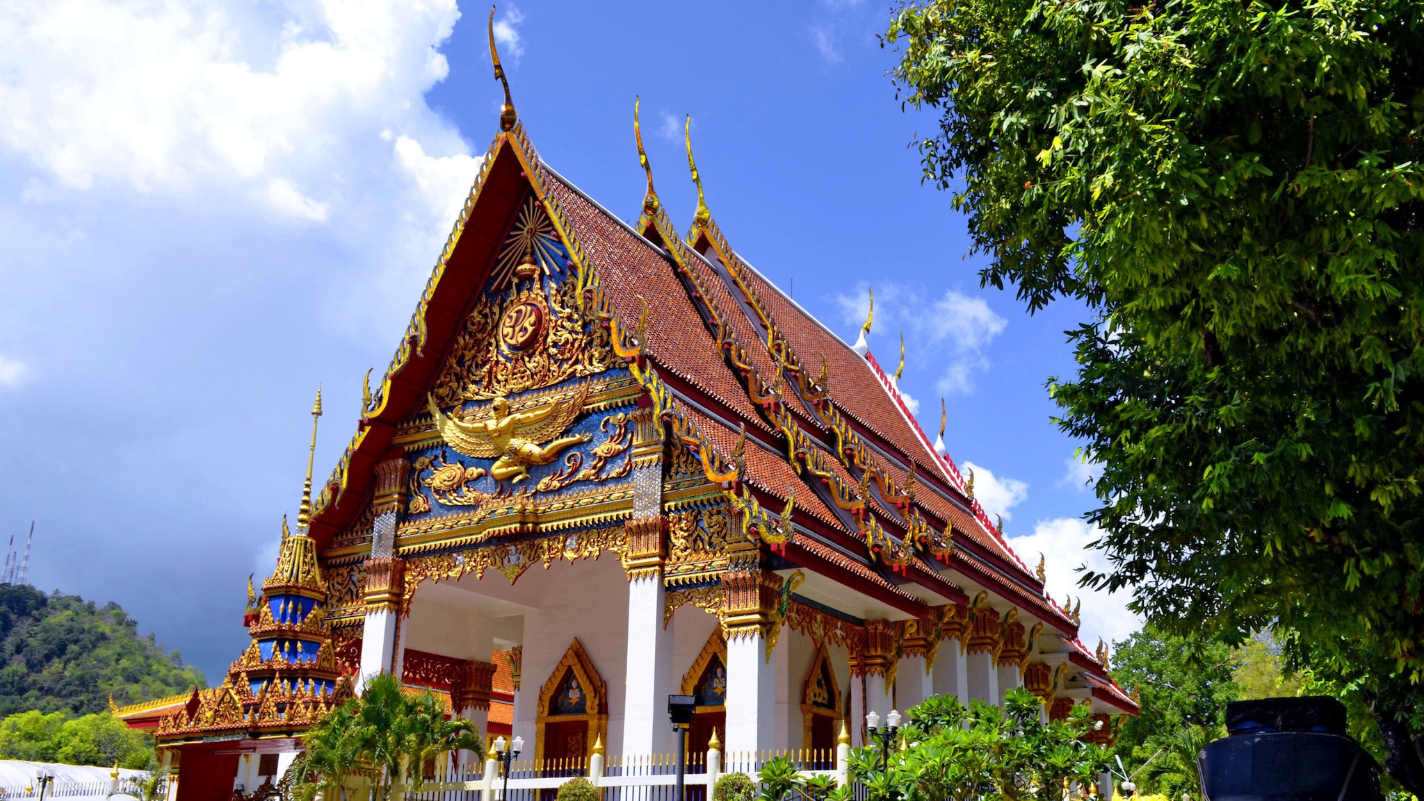 amex-magazin-geheimtipps-phuket-tempel Ein weißer Tempel mit Spitzdach, der mit üppiger bunter Dekoration und goldenen Elementen geschmückt ist.