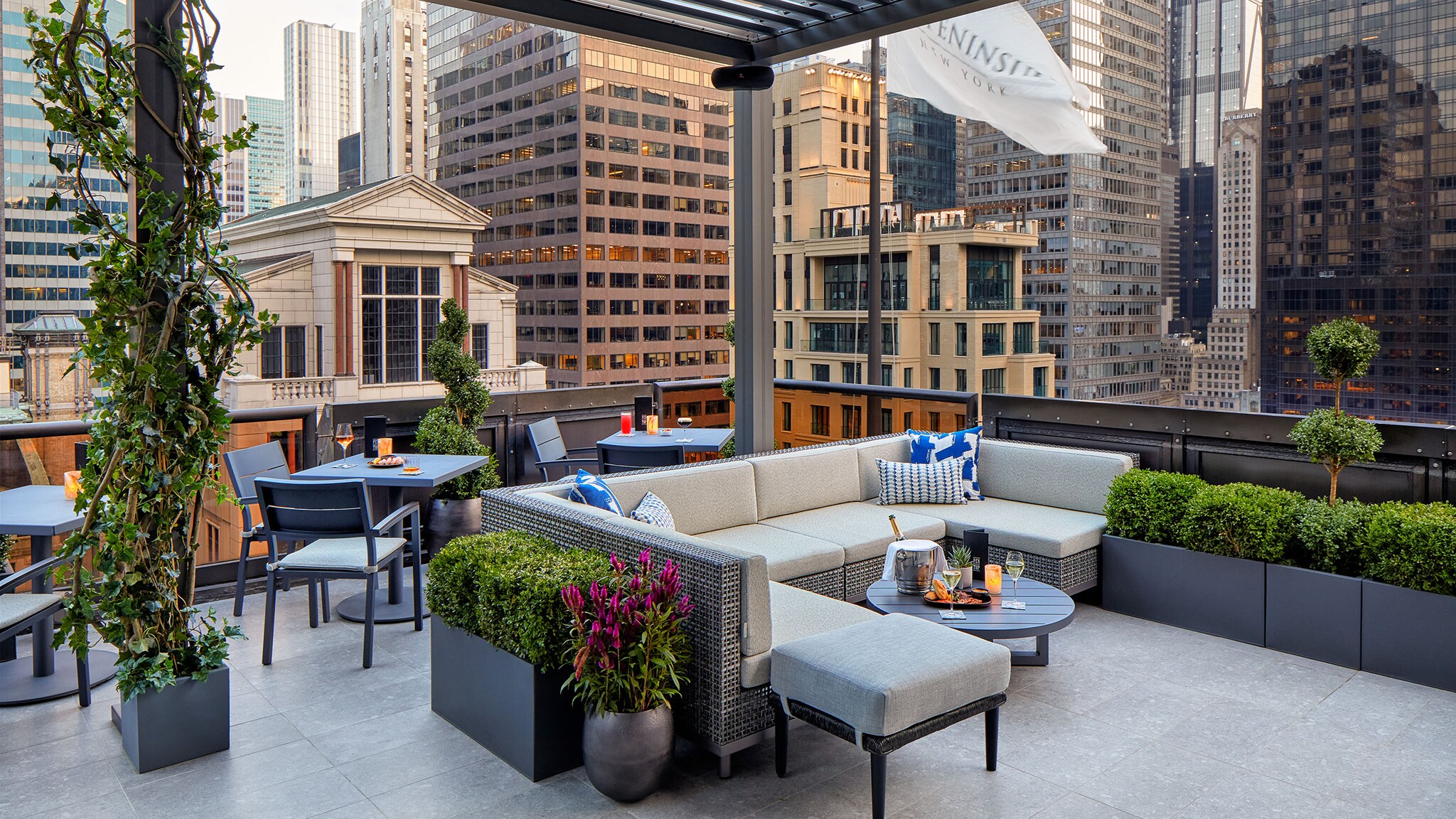 Luxuriöse Hotelterrasse mit Lounge-Bereich vor Skyline mit unterschiedlichen Hochhäusern im Stadtzentrum von New York.