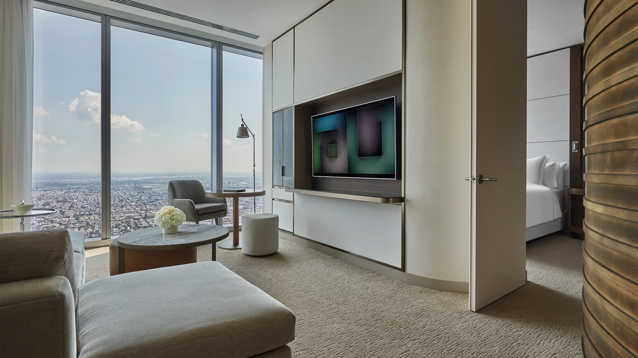 Helle, moderne Hotelsuite mit Panoramablick auf eine Stadt durch bodentiefe Fenster.