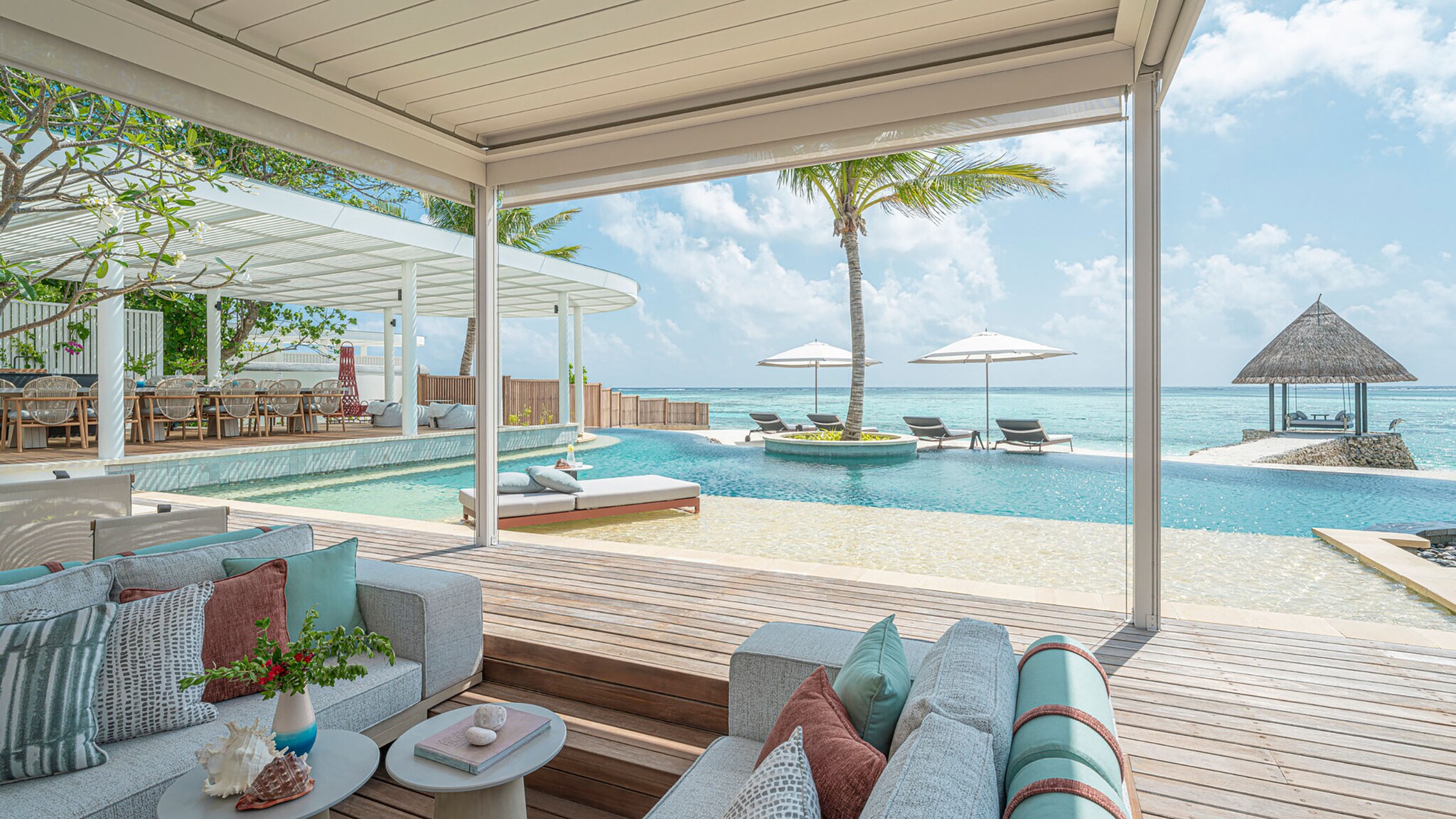 An einem Pool stehen Sonnenliegen und Stühle neben Palmen.