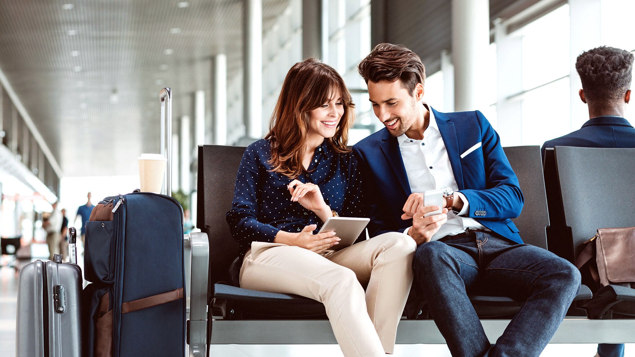 Ein Paar sitzt in einer Flughafenhalle und schaut auf ein Smartphone.