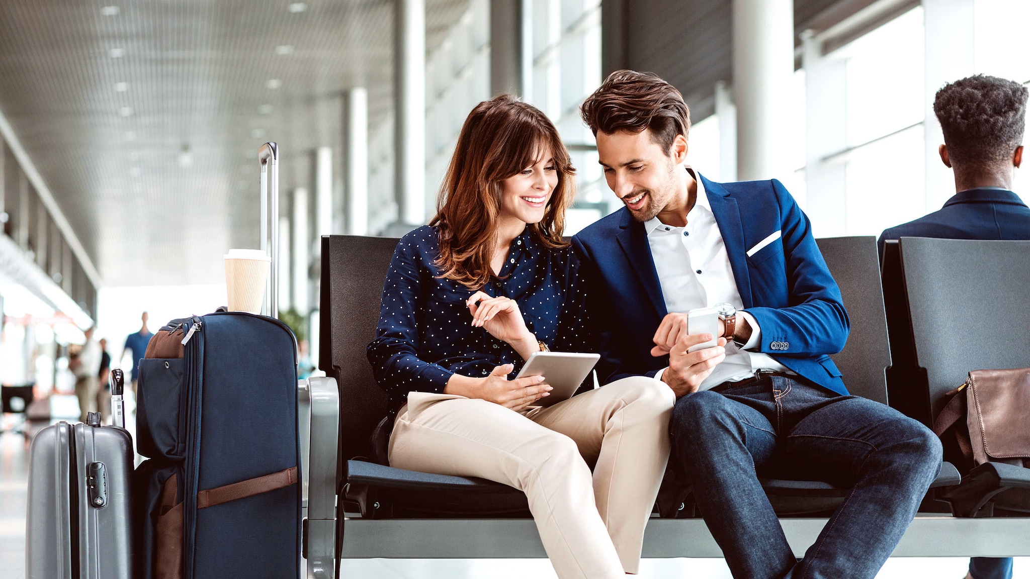Ein Paar sitzt in einer Flughafenhalle und schaut auf ein Smartphone.