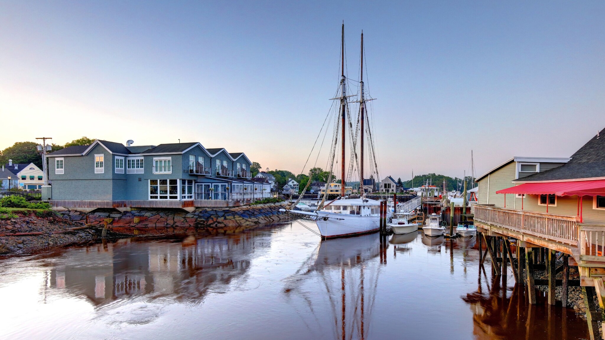 Segelboote in einem kleinen Hafen mit blauen Holzhäusern bei Abenddämmerung. Segelboote in einem kleinen Hafen mit blauen Holzhäusern bei Abenddämmerung.