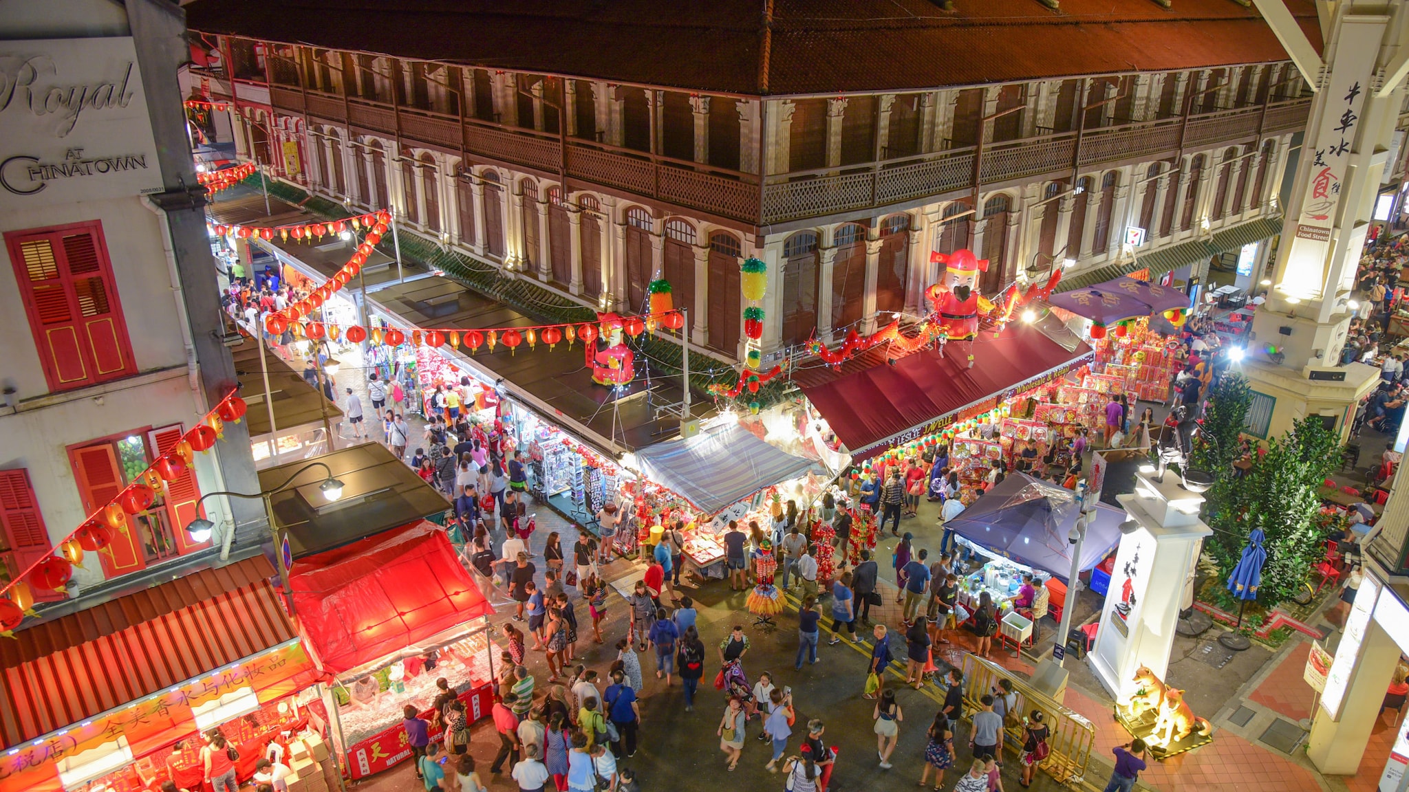 Aufsicht einer belebten Straßenkreuzung mit beleuchteten Marktständen und chinesischen Lampions in einem Stadtzentrum bei Nacht.