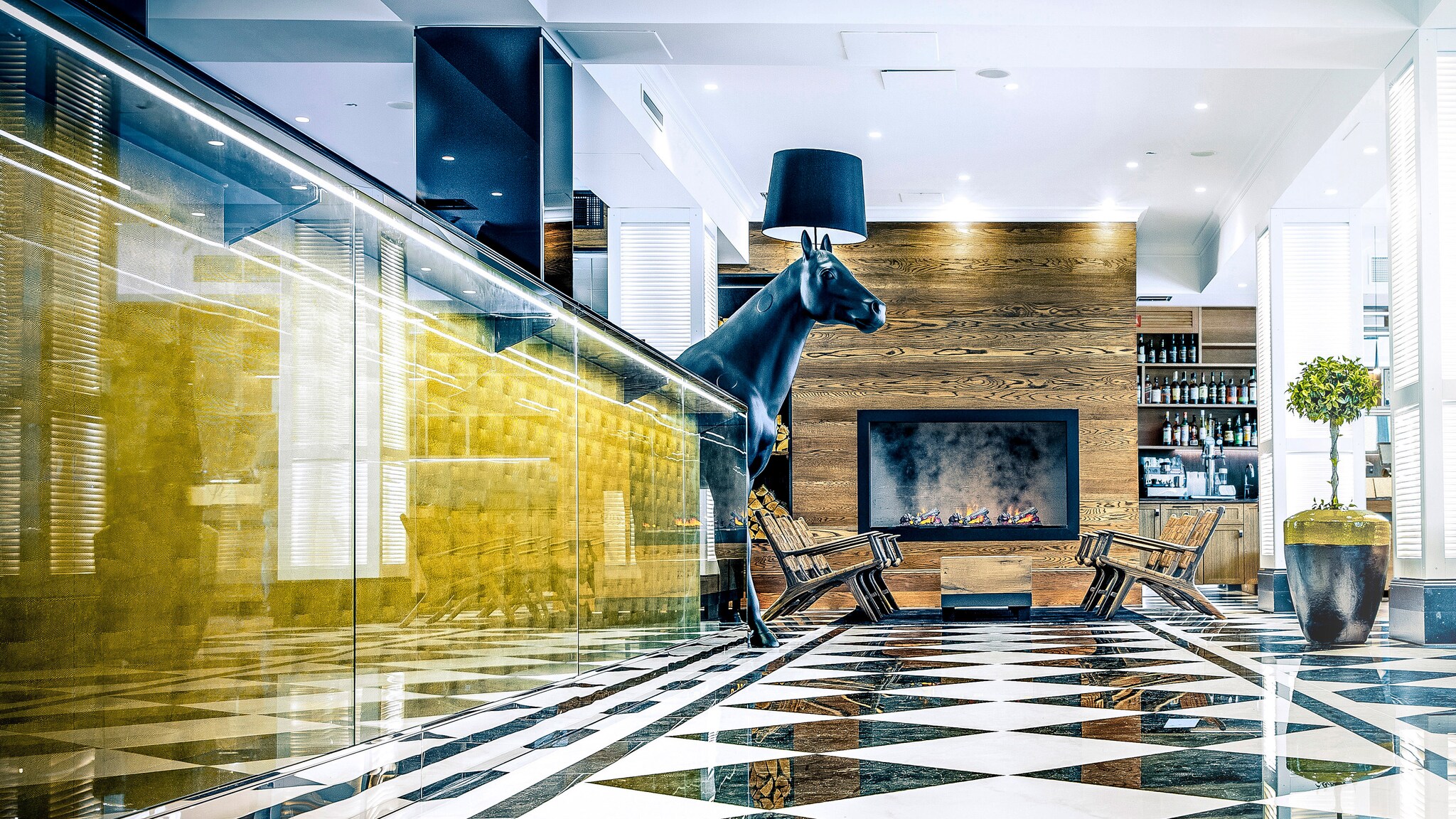 Moderne Hotellobby mit gläsernem Tresen, offenen Kamin und großer Pferde-Skulptur.