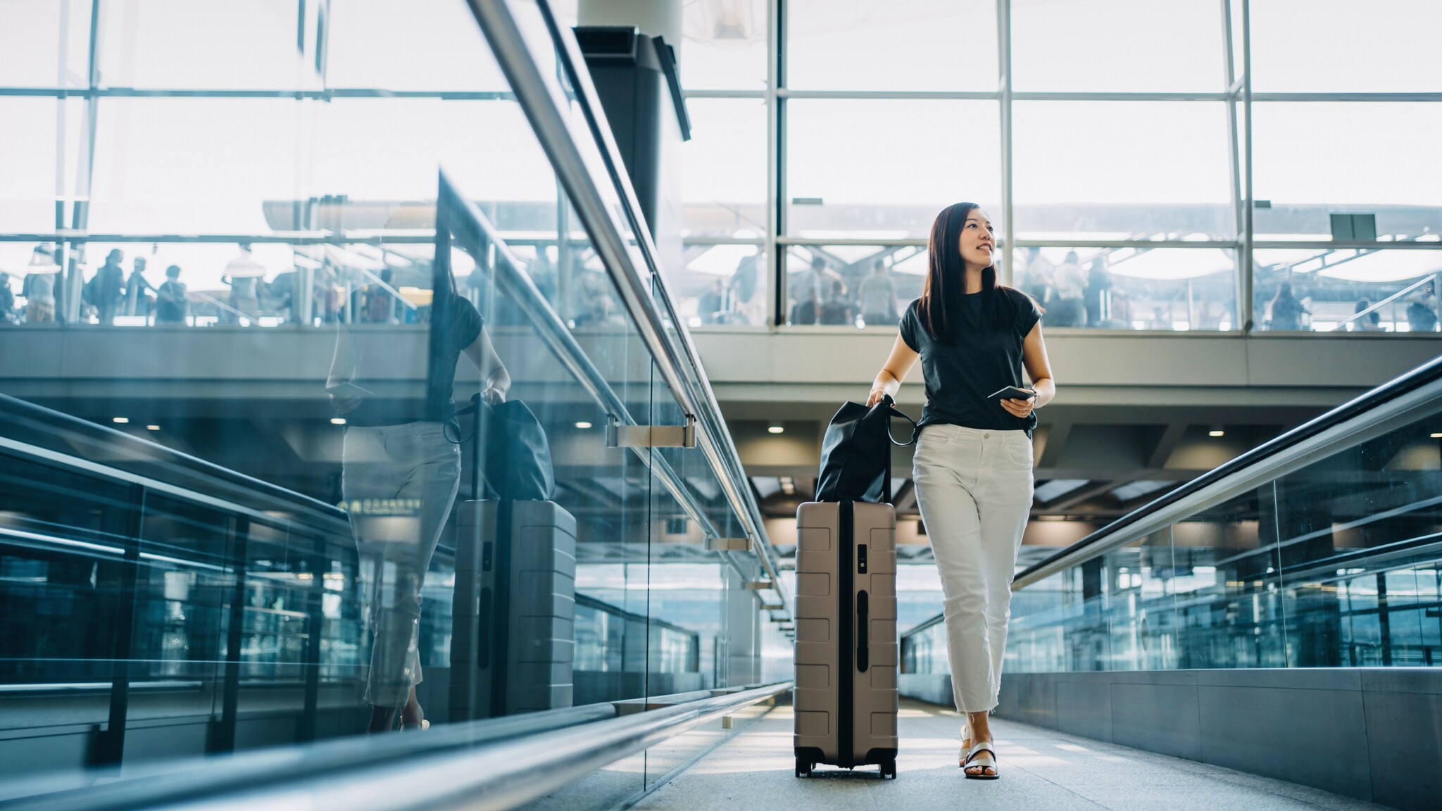Eine Frau läuft mit Rollkoffer durch einen Flughafenterminal.