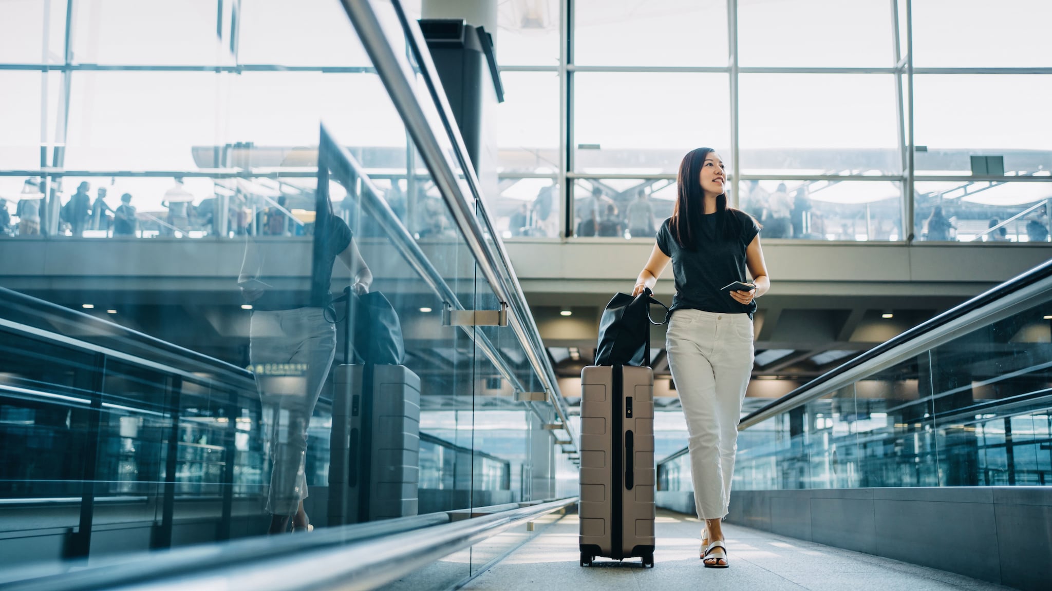 amex-sbs-american-express-gold-business-versicherung-frau-koffer Eine Frau läuft mit Rollkoffer durch einen Flughafenterminal.