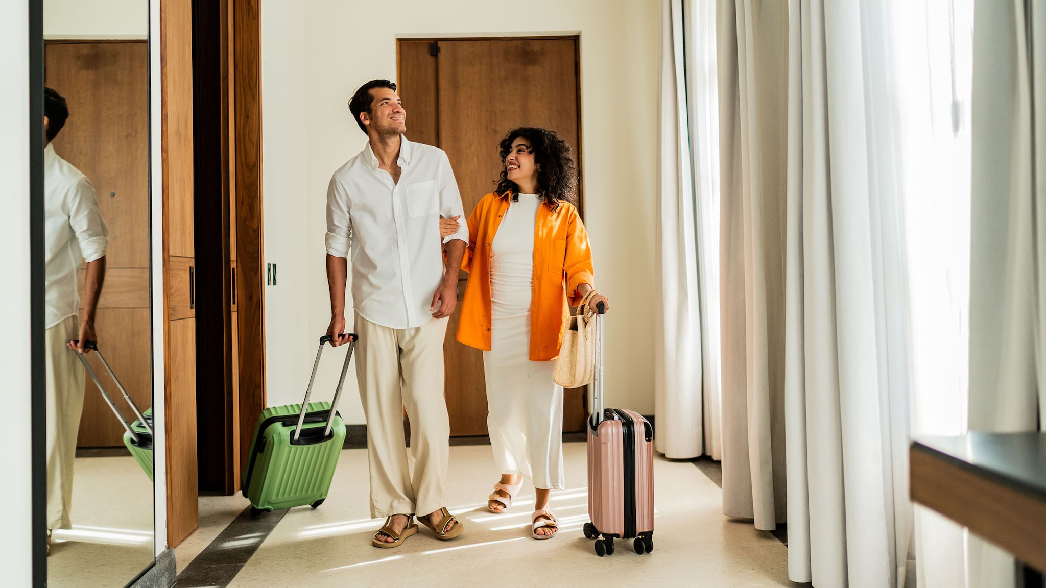 AMEX Hotels Ein Mann und eine Frau gehen eingehakt und lächelnd mit Trolleys im Eingangsbereich eines Hotelzimmers.