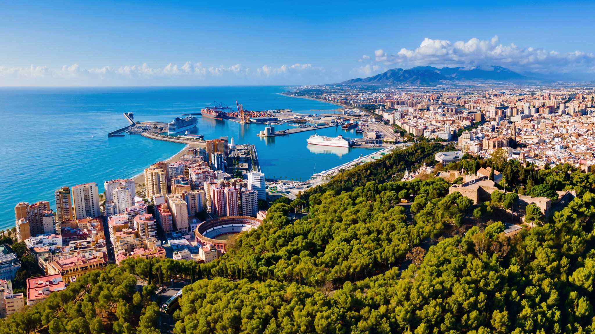 Luftaufnahme von Málaga am Meer mit Hafen und Waldgebiet.
