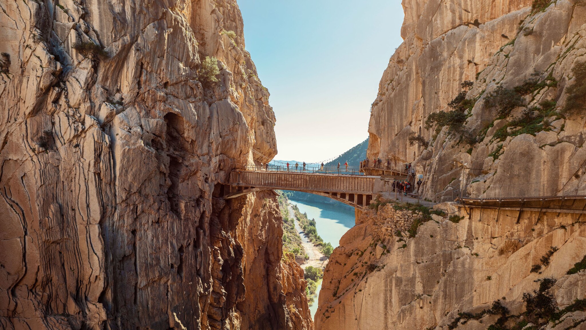 amex-magazin-malaga-urlaub-holzbruecke-felswaende Personen laufen auf einer schmalen Holzbrücke zwischen zwei Felswänden an einer Schlucht.