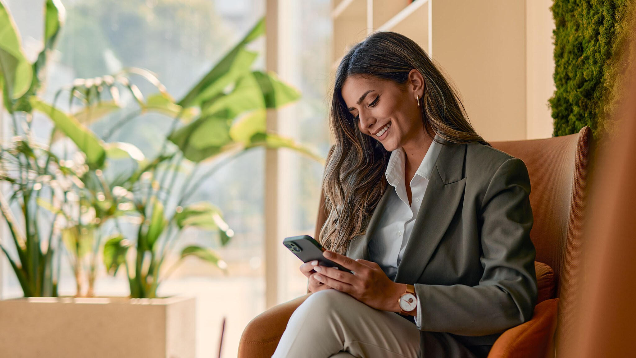 Eine Frau sitzt auf einem Sessel und schaut auf ihr Smartphone.
