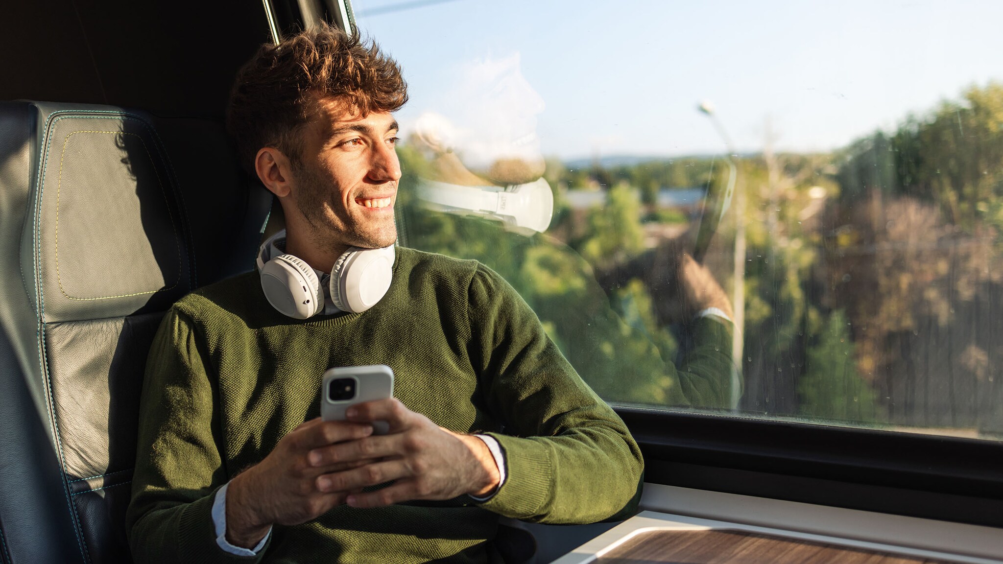 Ein Mann sitzt im Zug und hält sein Smatphone in der Hand.