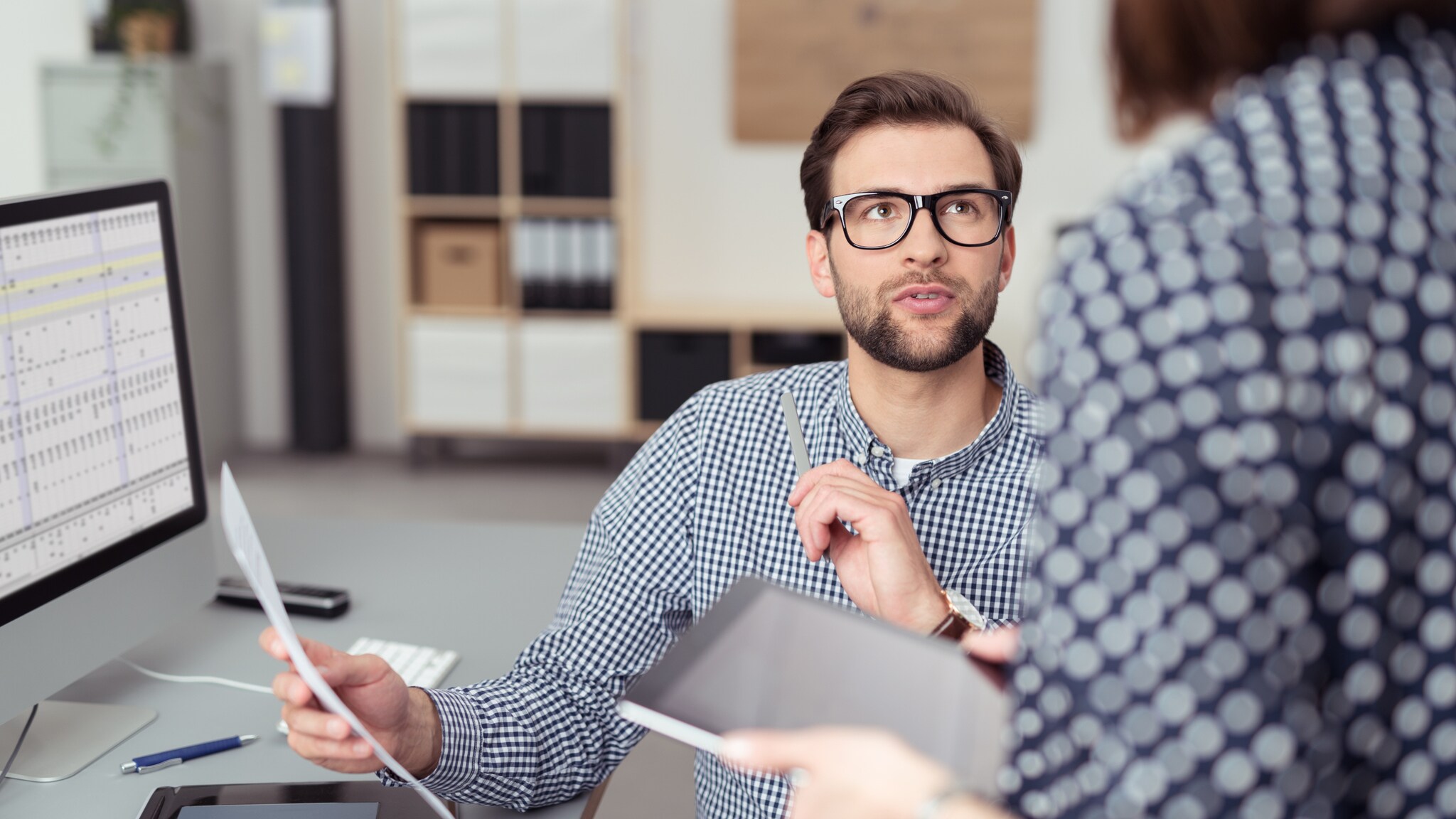 Ein Mann sitzt an seinem Büroschreibtisch und bespricht angeregt etwas mit einer Frau mit Tablet in den Händen