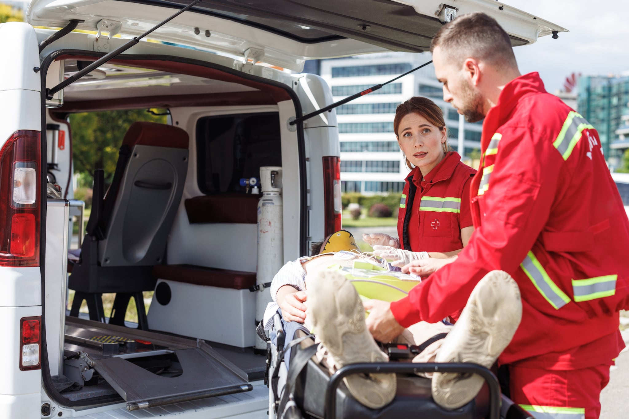 amex-insurances-krankenruecktransport-krankenwagen Zwei Sanitäter:innen bringen eine verletzte Person auf einer Liege in einen Krankenwagen.