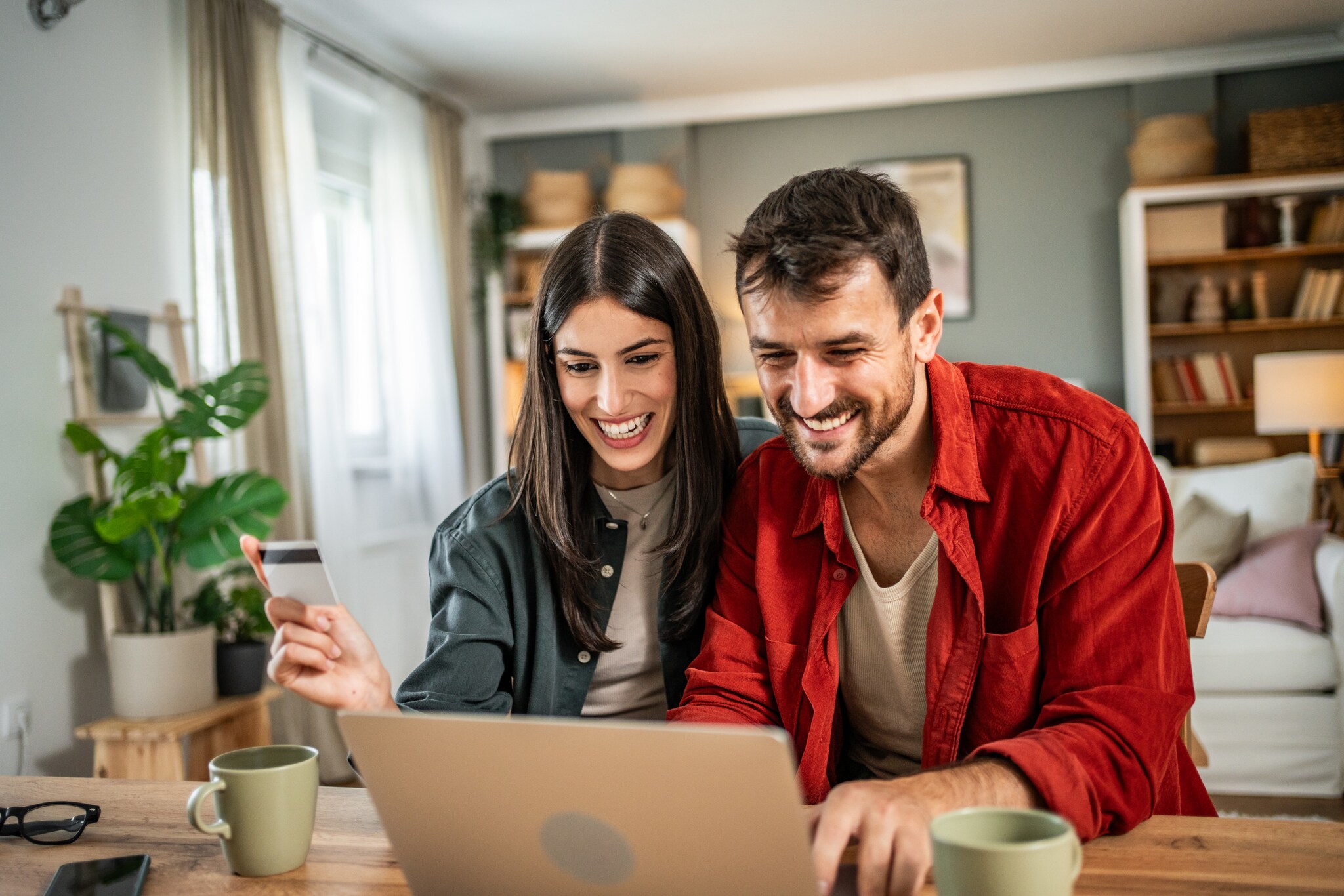 Ein Mann und eine Frage schauen lachend auf einen Bildschirm, in der Hand hält sie eine Bezahlkarte.
