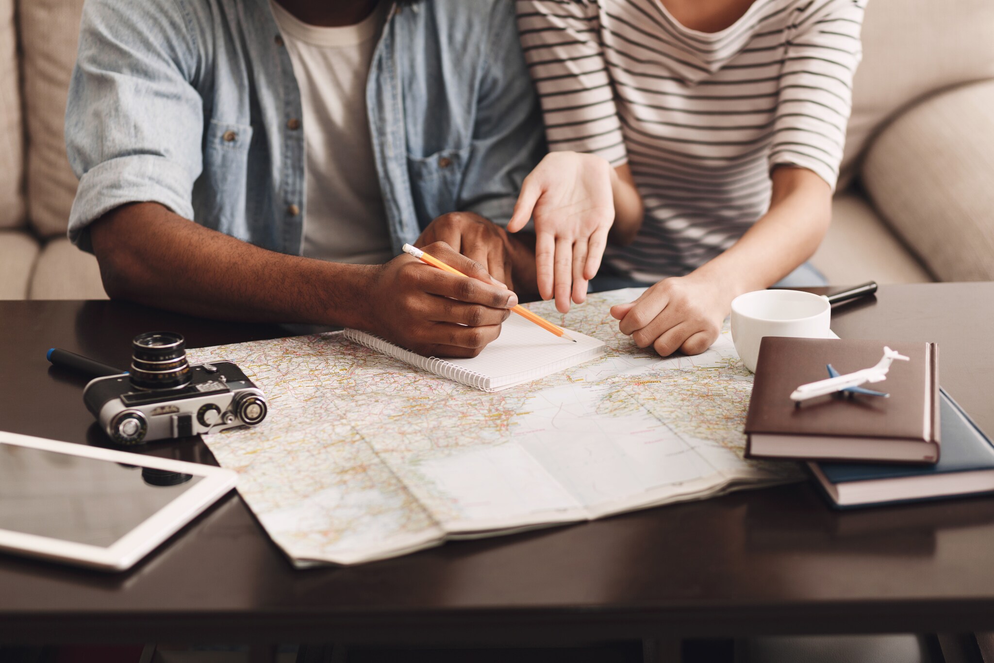 Ein Paar sitzt vor einer Landkarte, plant seinen Urlaub und macht sich Notizen.