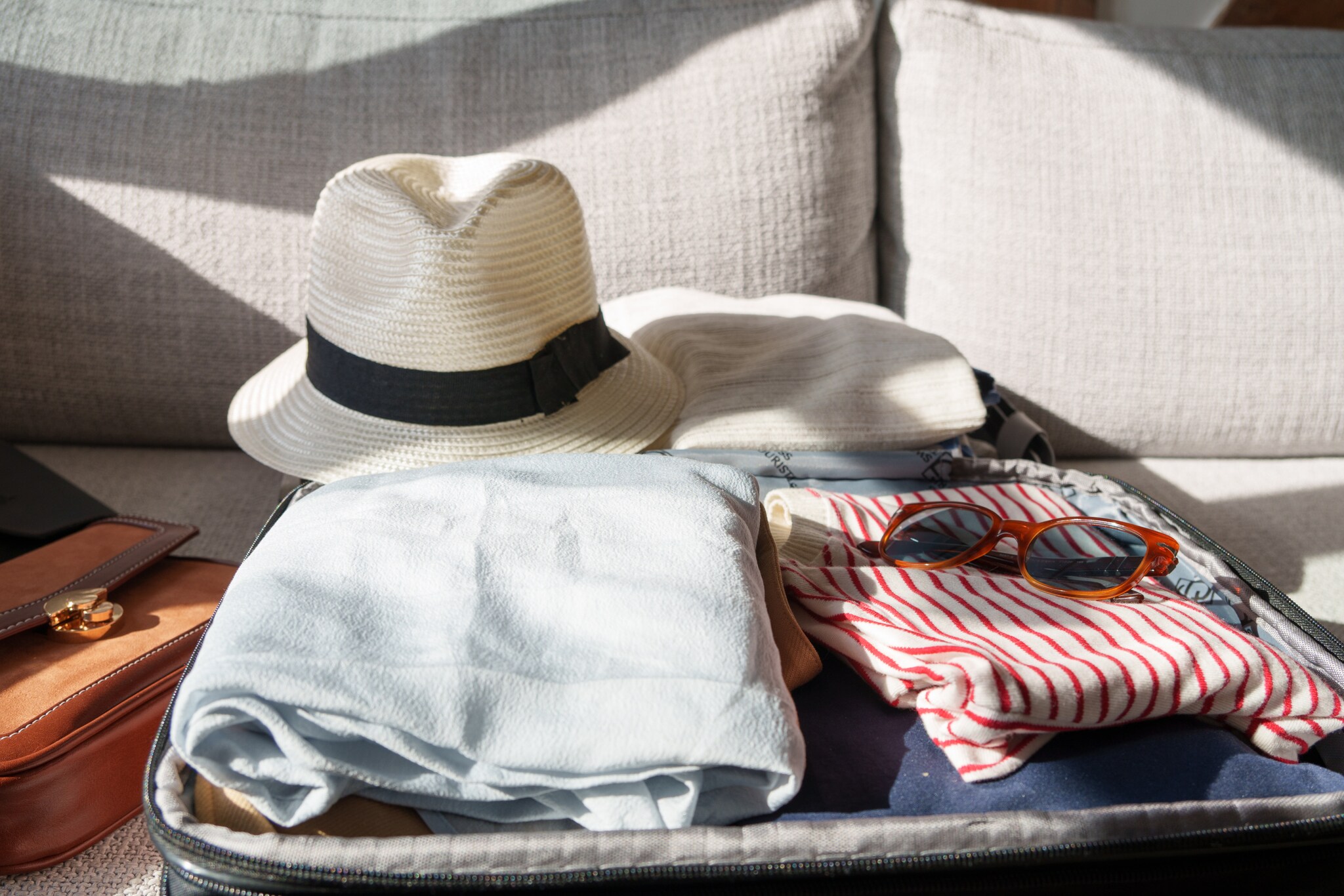 Ein offener, gepackter Koffer mit Sonnenbrille und Hut liegt auf einem Sofa.
