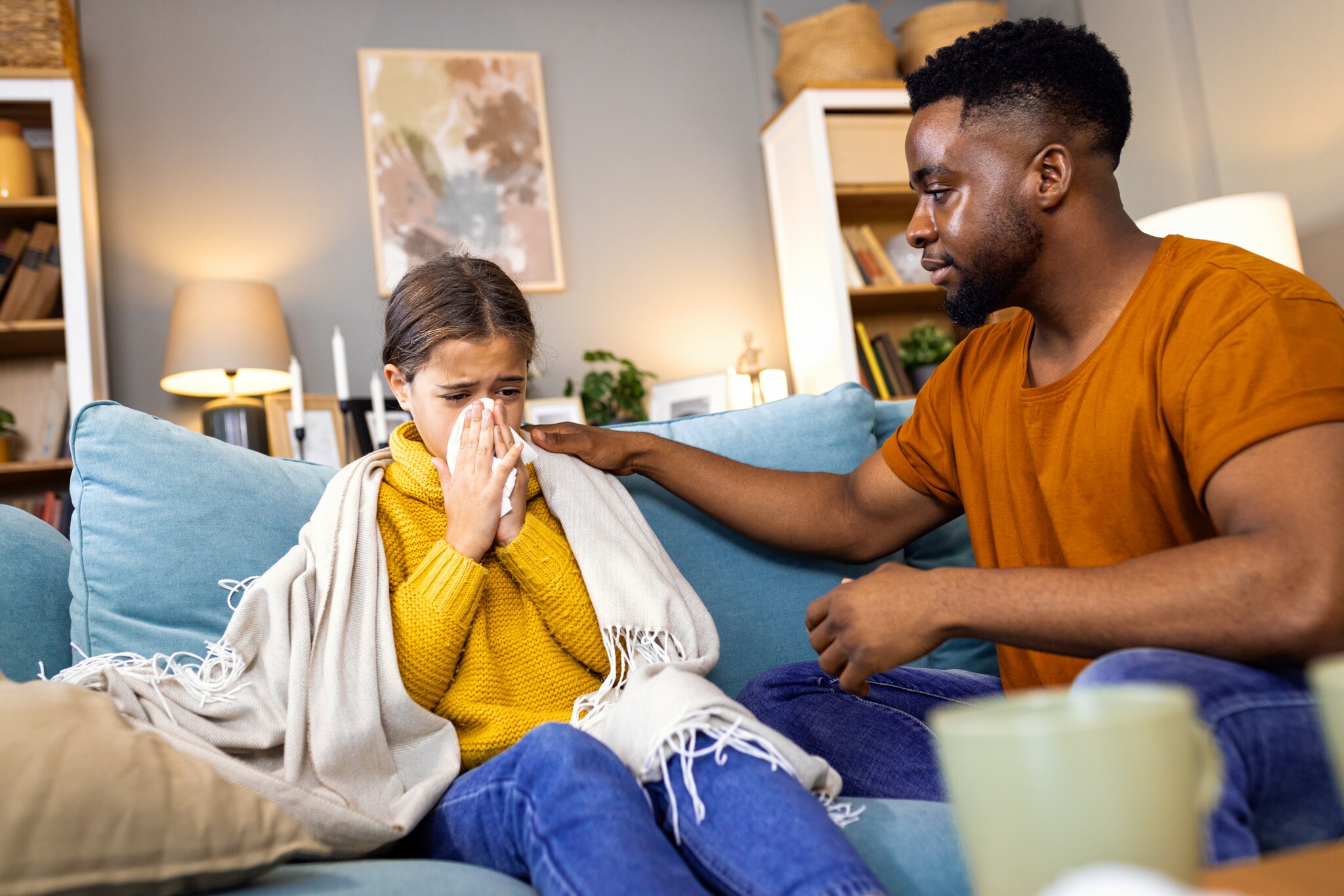 Ein Man sitzt neben einem kranken Kind auf dem Sofa und legt ihm die Hand auf die Schulter.