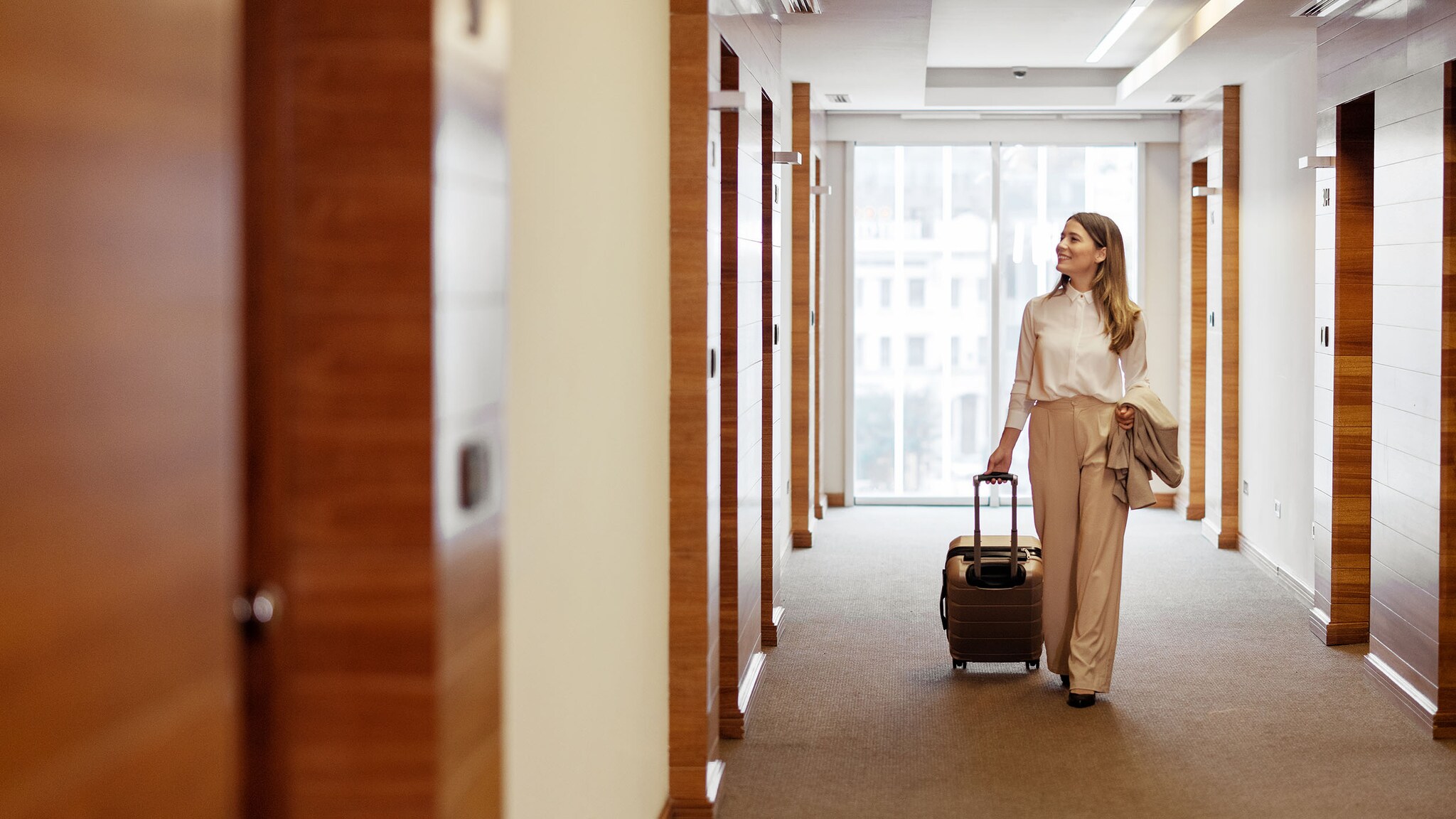 Eien Frau geht mit ihrem Koffer einen Hotelflur entlang.