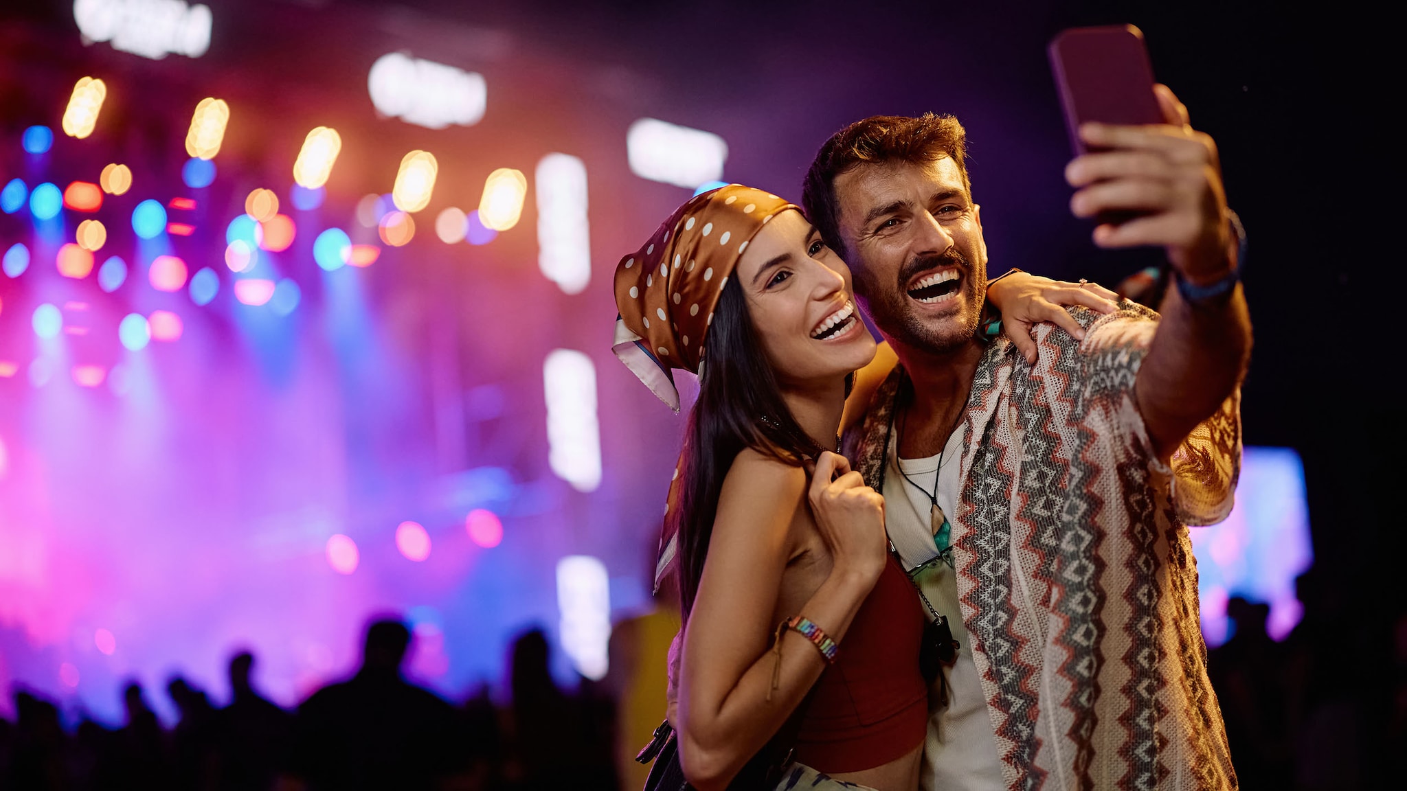 Ein Mann und eine Frau stehen vor einer Bühne und machen ein Selfie.