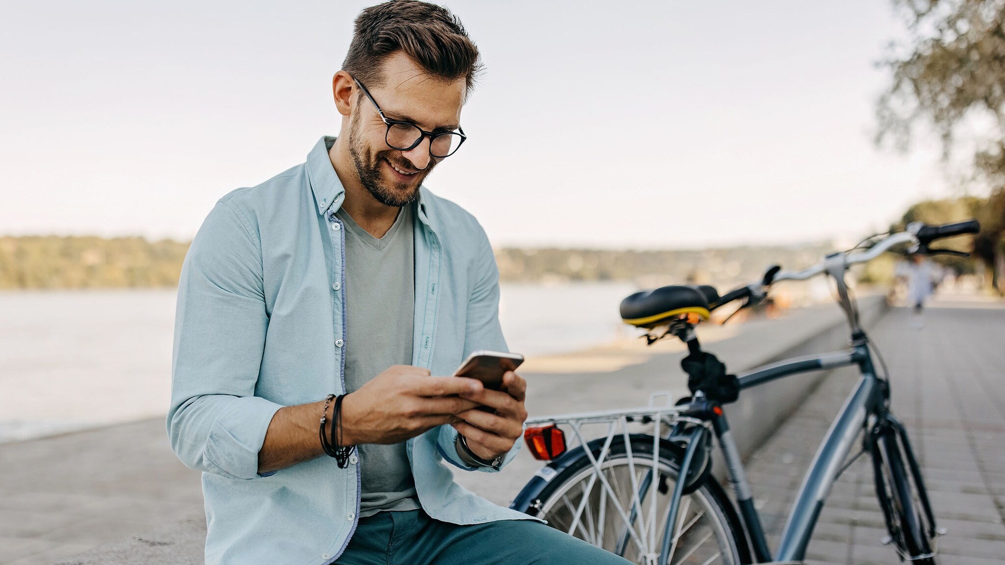 Ein Mann sitzt neben seinem Fahrrad und schaut auf sein Smartphone.