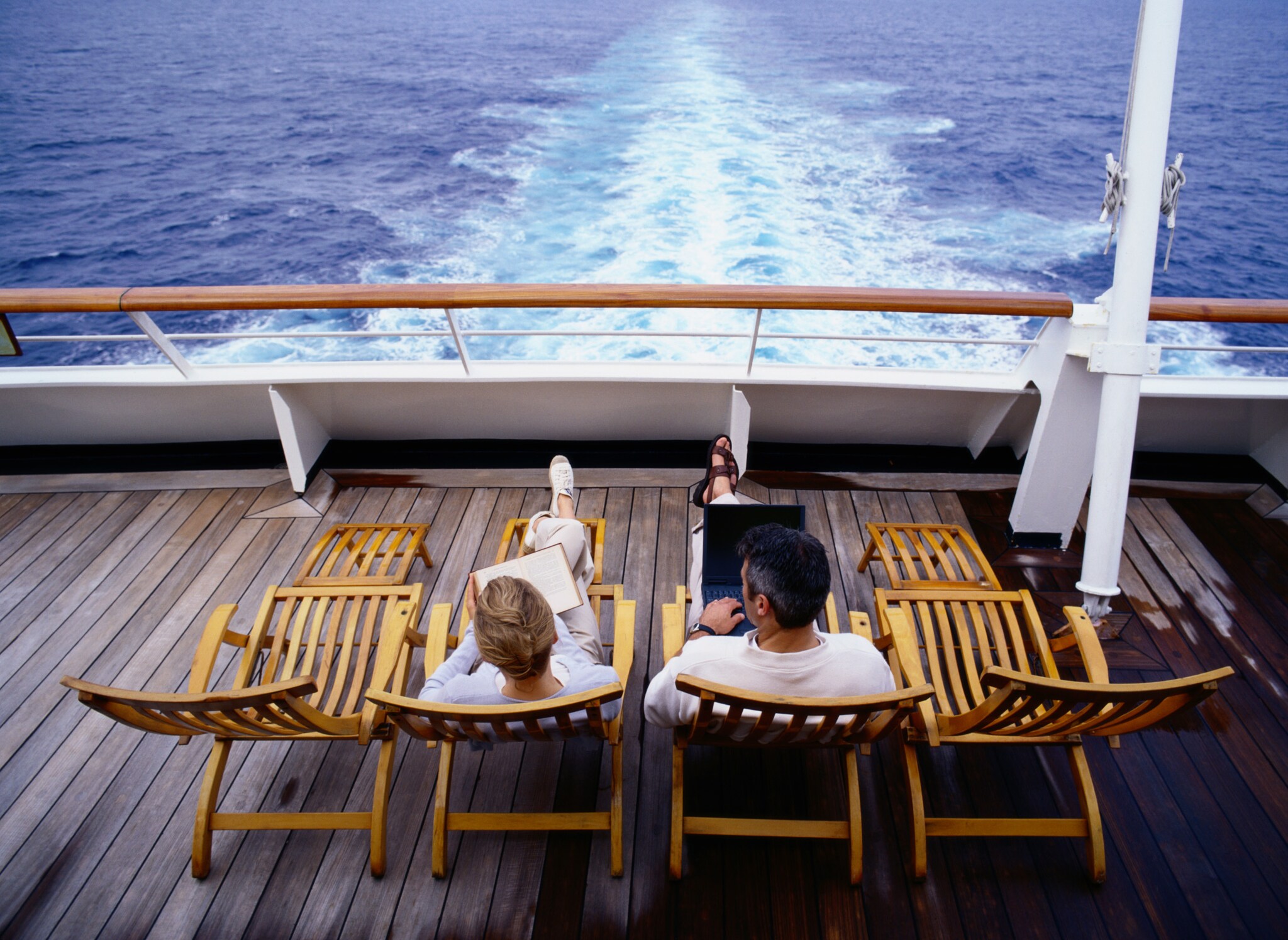 Ein Pärchen liegt auf Liegestühlen auf einem Schiffsdeck, vor ihnen das Meer.