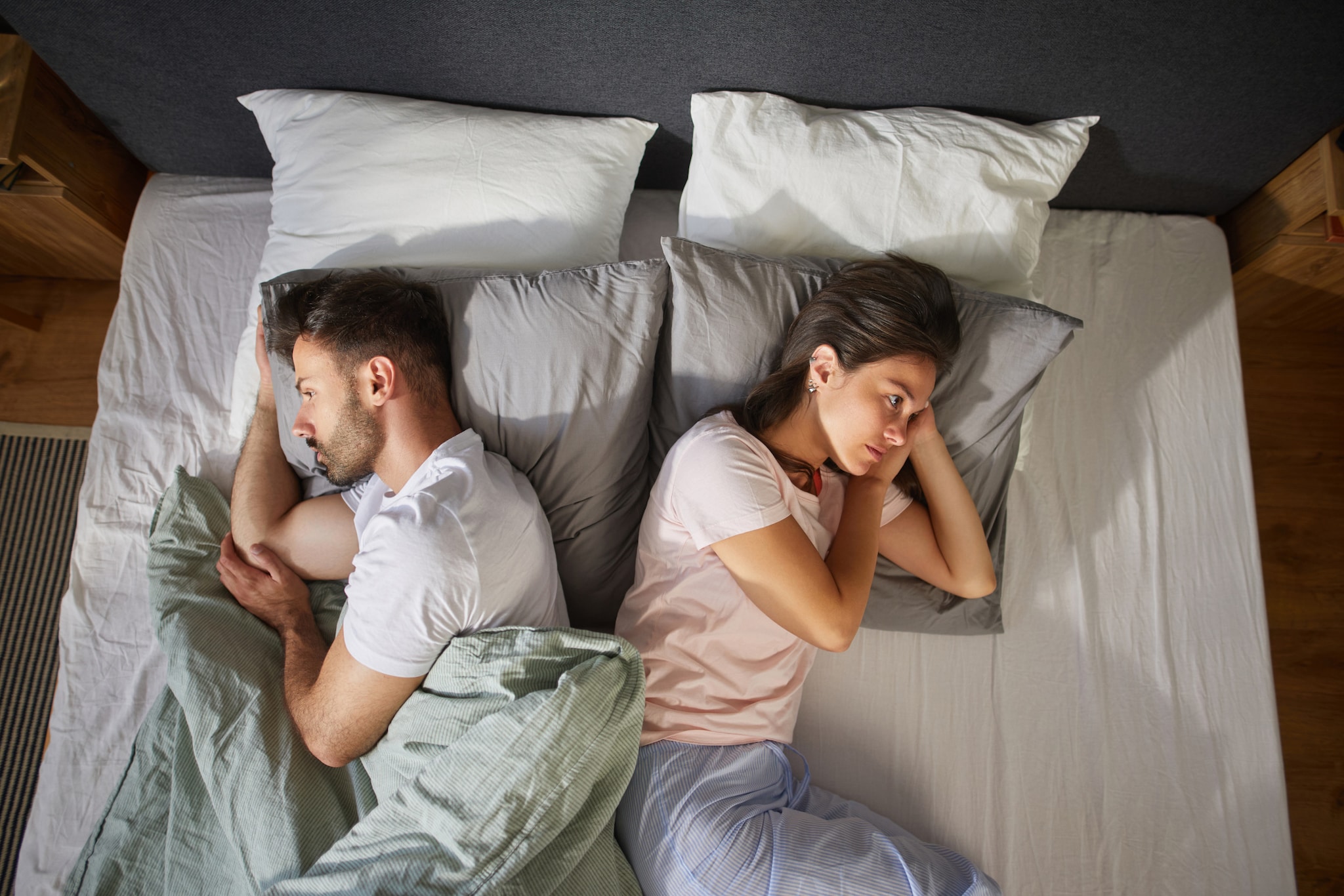 amex-insurances-reiseruecktrittsversicherung-bei-trennung-mann-frau-bett Ein Mann und eine Frau liegen voneinander abgewandt in einem Bett und blicken traurig.