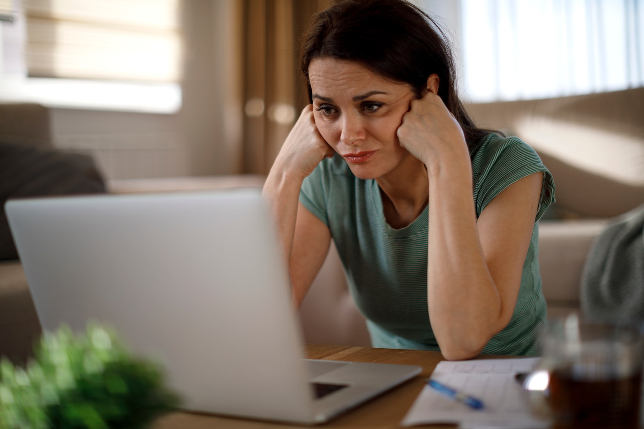 amex-insurances-reiseruecktrittsversicherung-flug-stornieren-frau-laptop Eine Frau sitzt vor einem Laptop. Sie stützt den Kopf in ihren Händen und guckt frustriert auf den Bildschirm.