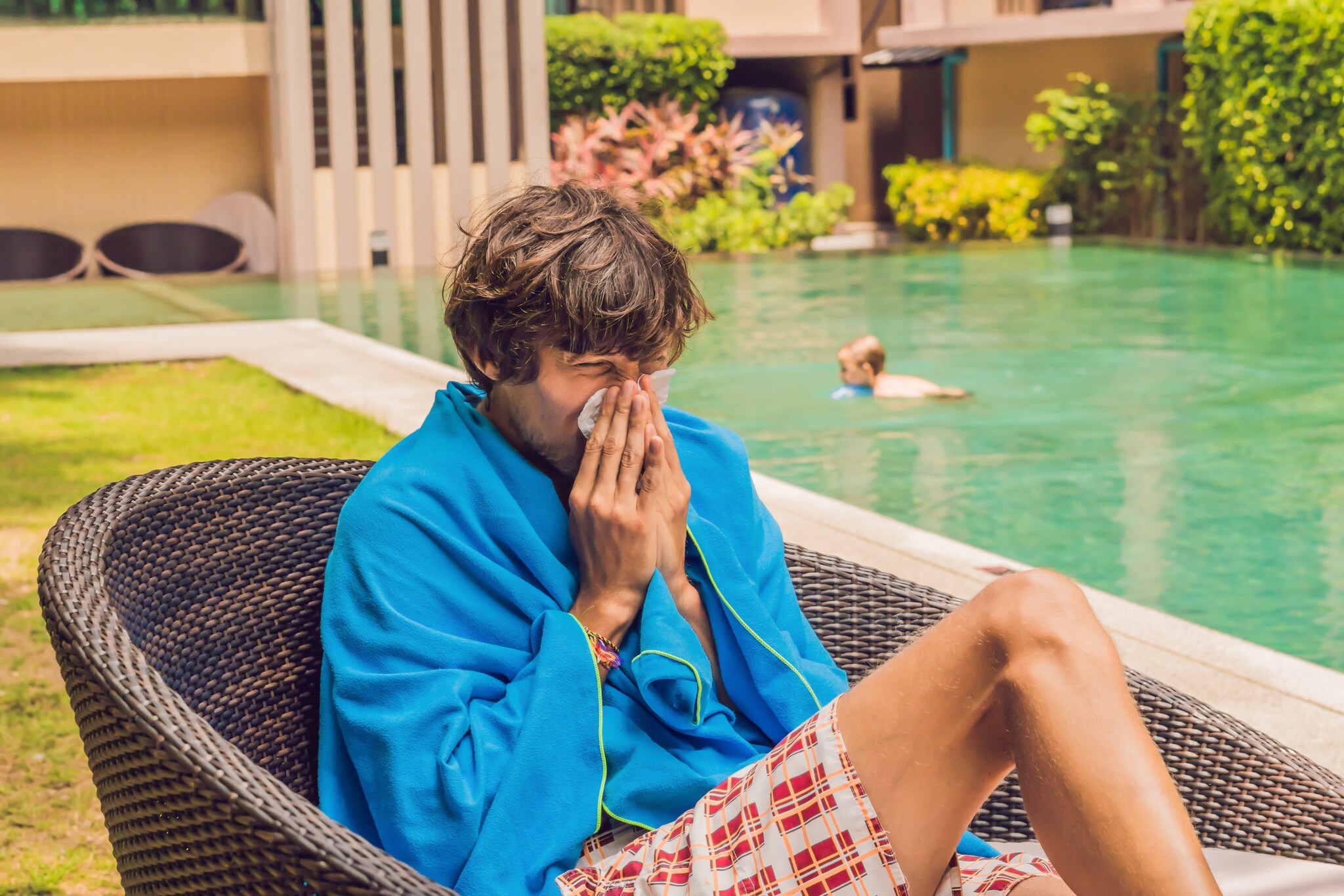 Ein Mann sitzt mit einer Decke am Pool und schnäuzt sich die Nase.