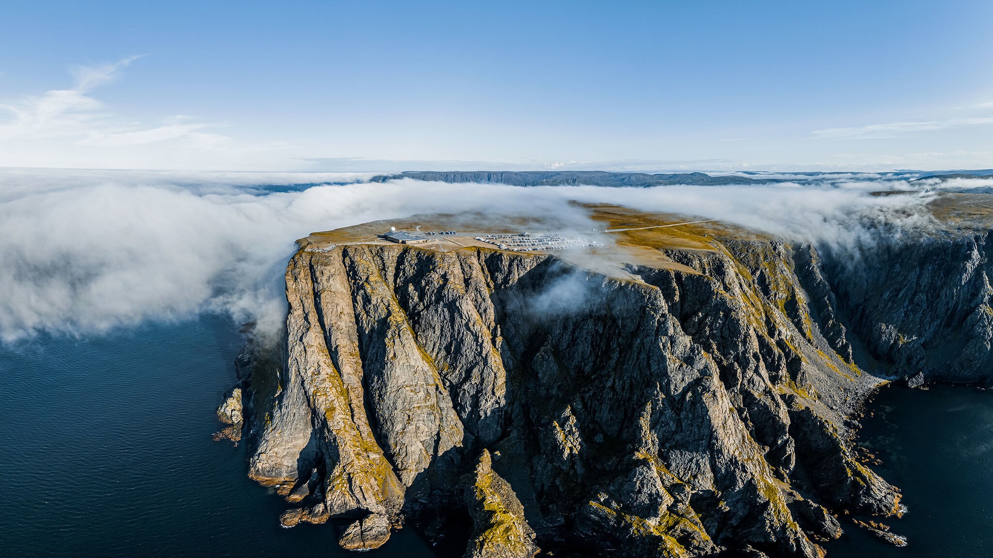 Aus dem Meer ragen sehr hohe Klippen empor, auf der Spitze bilden sich Nebelwolken.