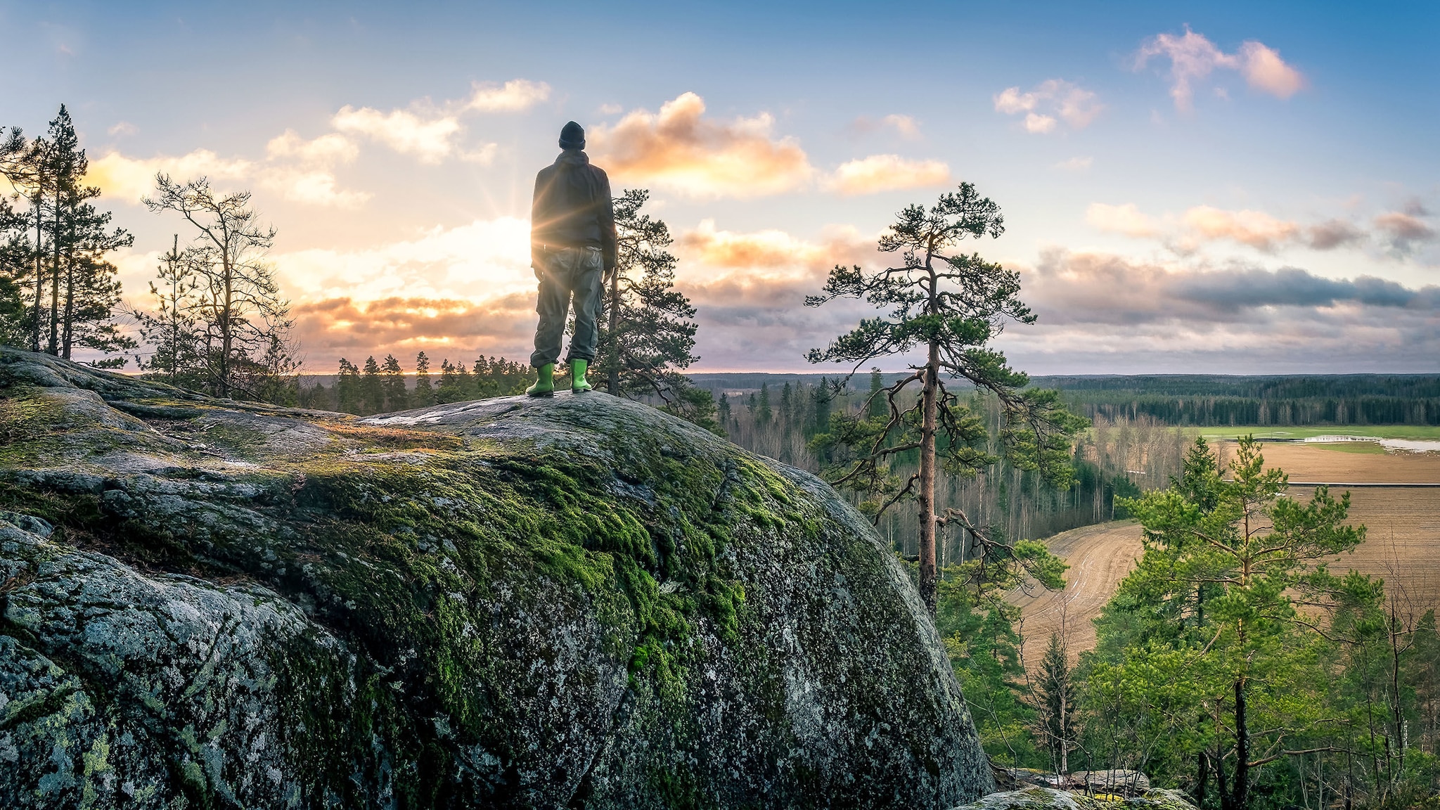Ein Mann steht auf einem Felsen, umgeben von Natur Ein Mann steht auf einem Felsen, umgeben von Natur