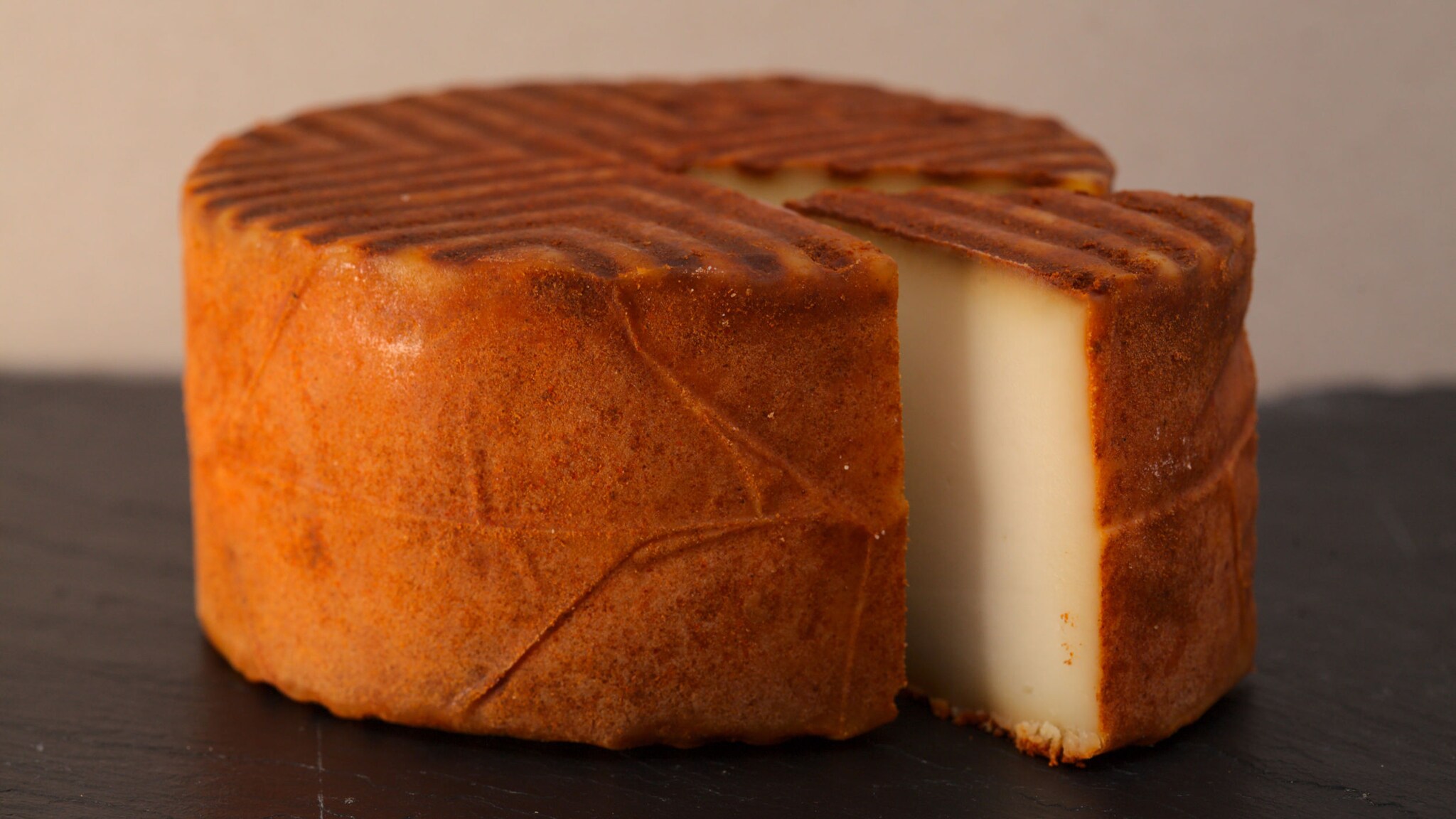 Ein angeschnittener runder Käselaib mit rötlich-brauner Rinde.