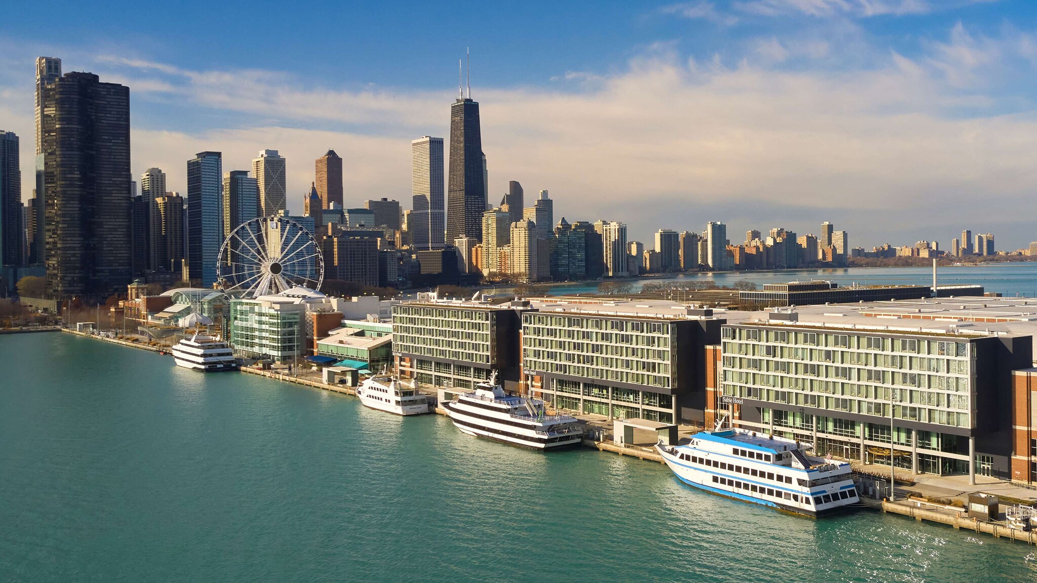 Kastenförmiger Hotelkomplex auf einer Landzunge mit Riesenrad an einer Waterfront vor der Skyline Chicagos. 