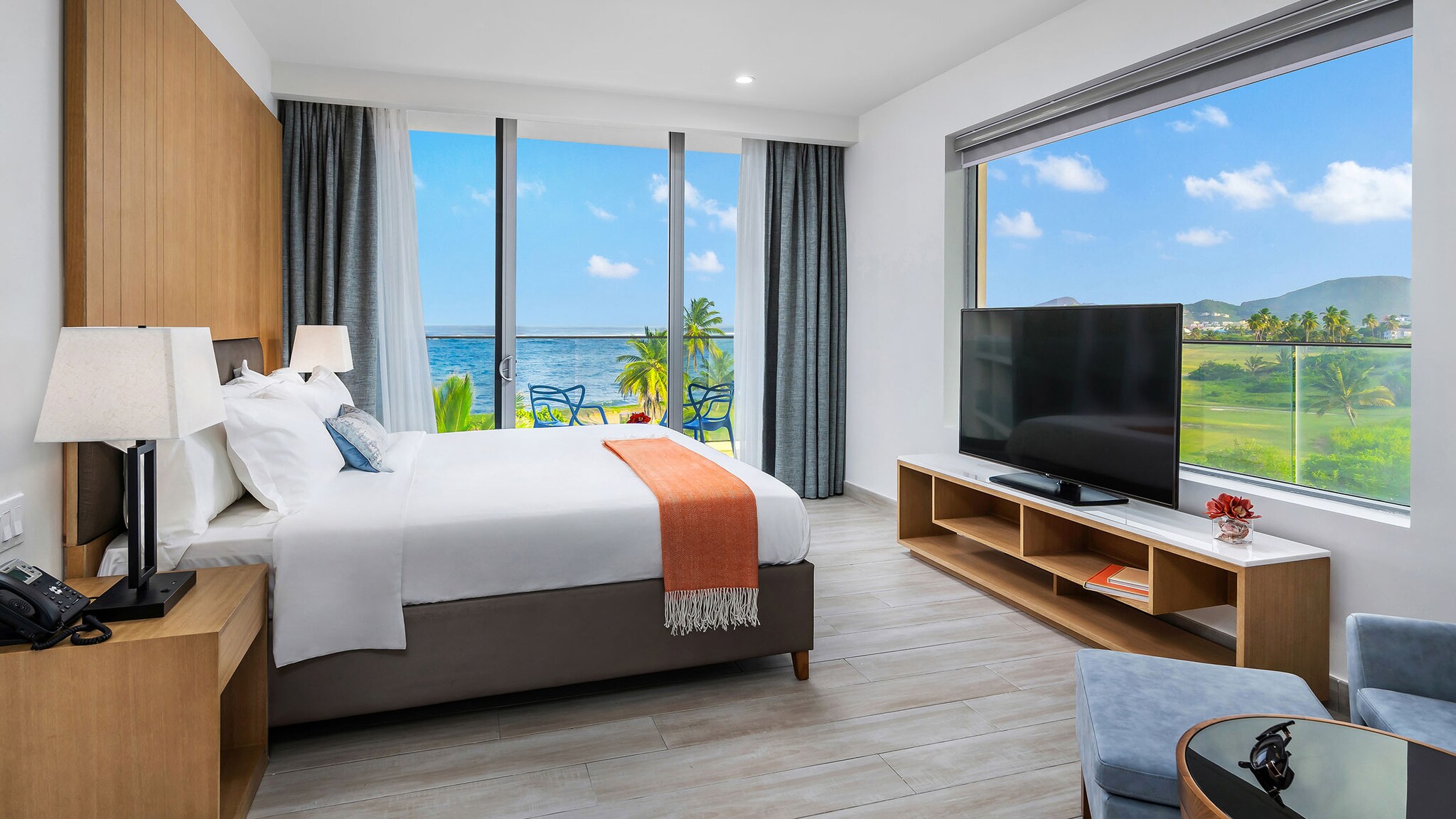 Hotelzimmer mit Doppelbett und Panoramafenstern mit Blick in tropische Landschaft am Meer.