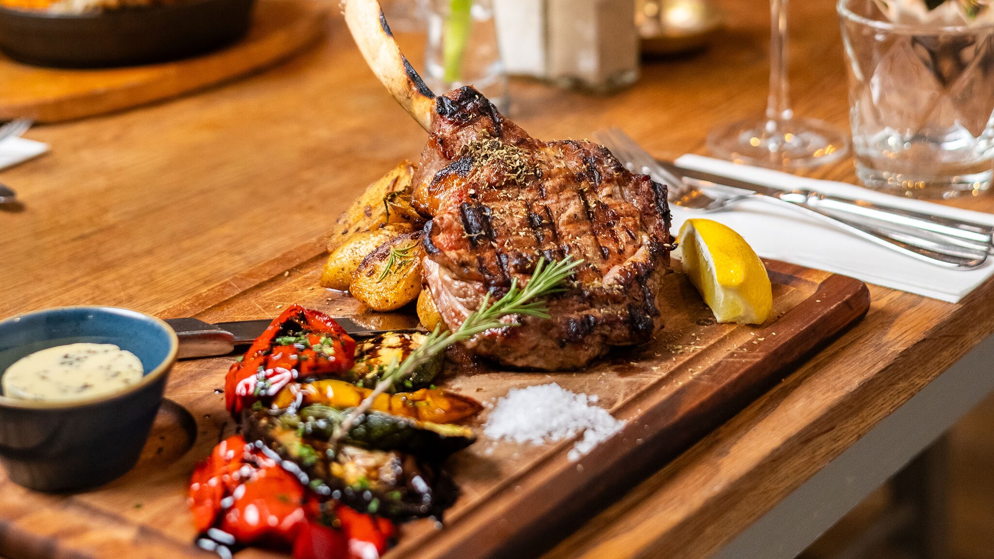 Ein Stück Fleisch und gebratene Paprika auf einem Holzbrett, garniert mit Gewürzen und Rosmarinzweig..