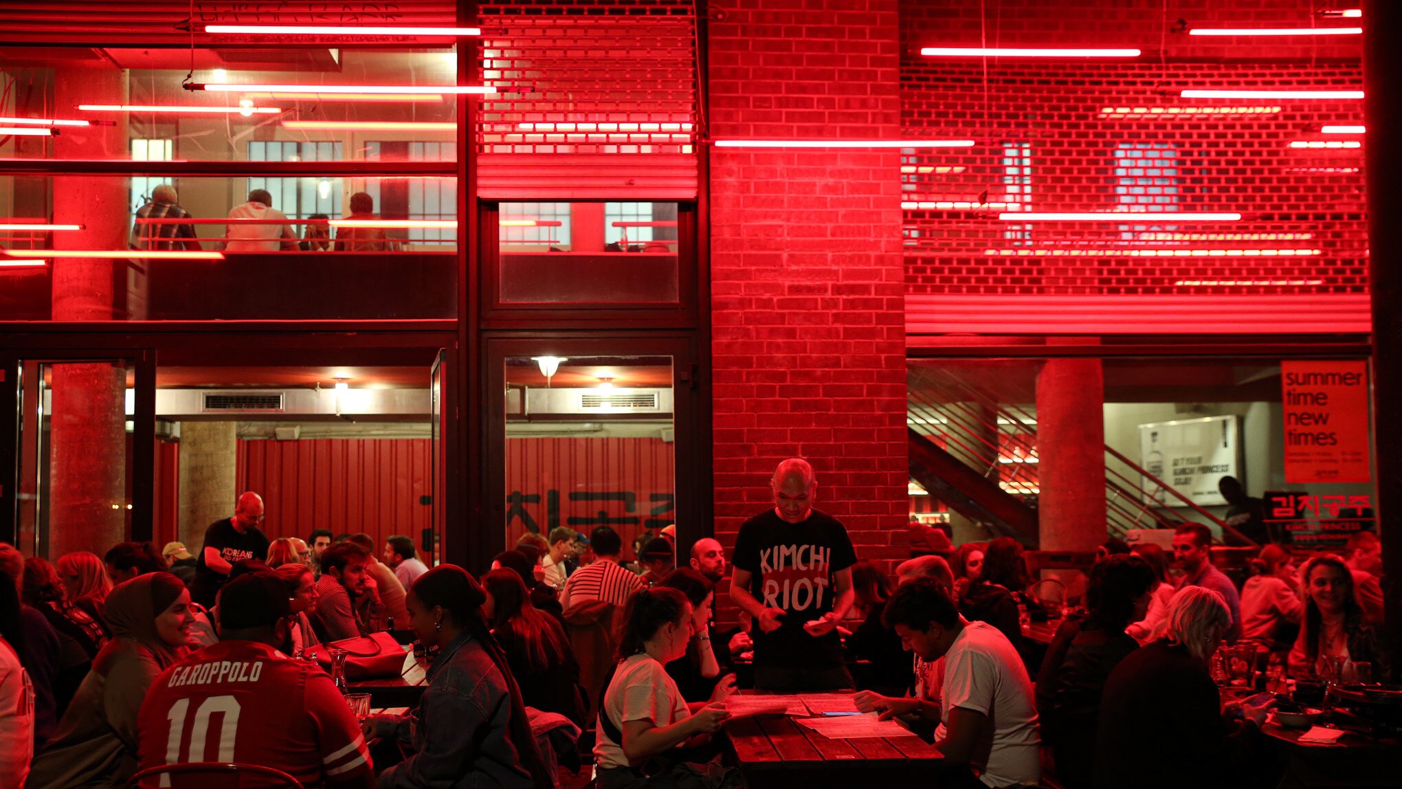 Voller Gastraum des Restaurants Kimchi Princess in dunkelrotem Licht und Industriestil.